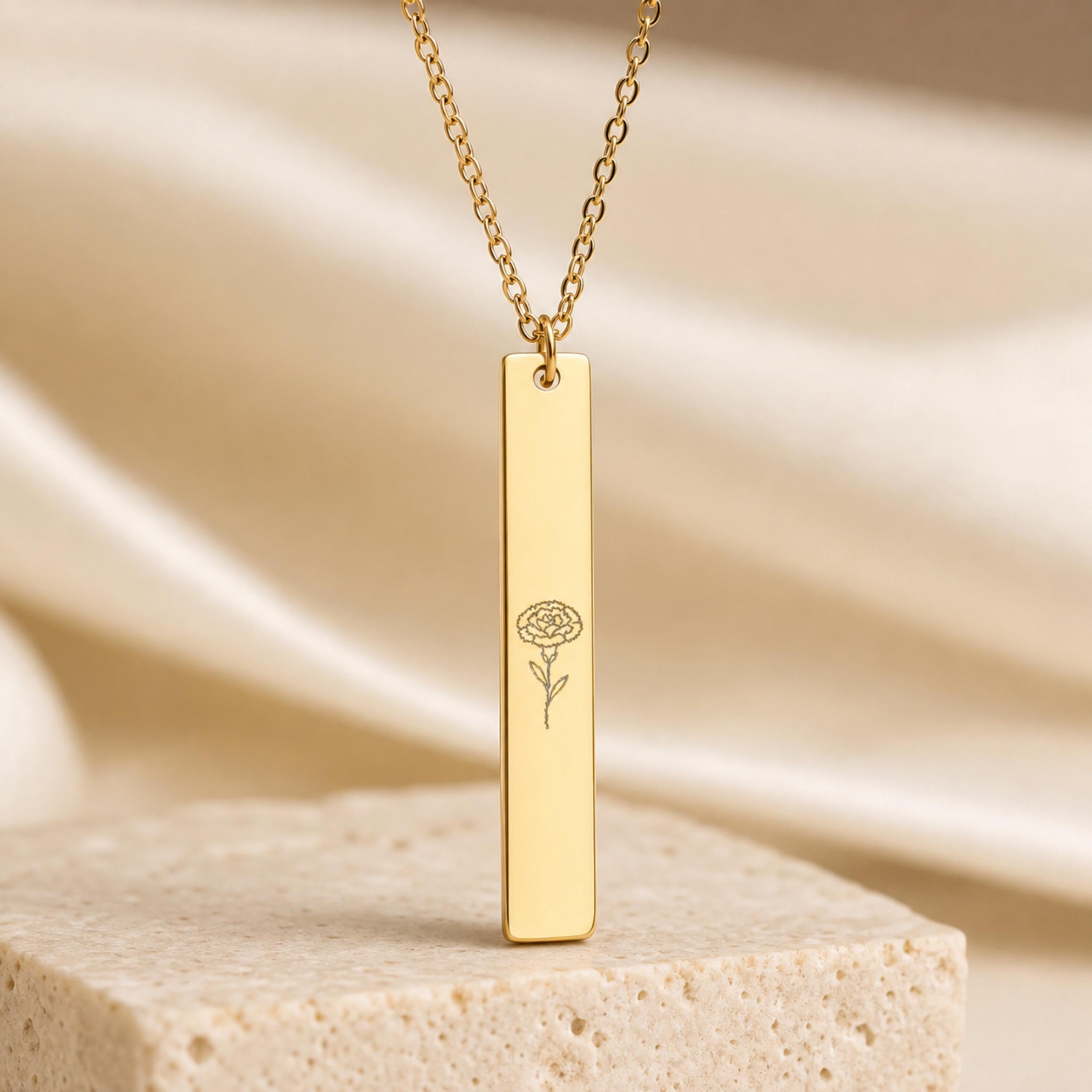 January birth flower necklace — Carnation engraved vertical bar pendant, 18K Gold PVD, premium pedestal product hero, 316L stainless steel
