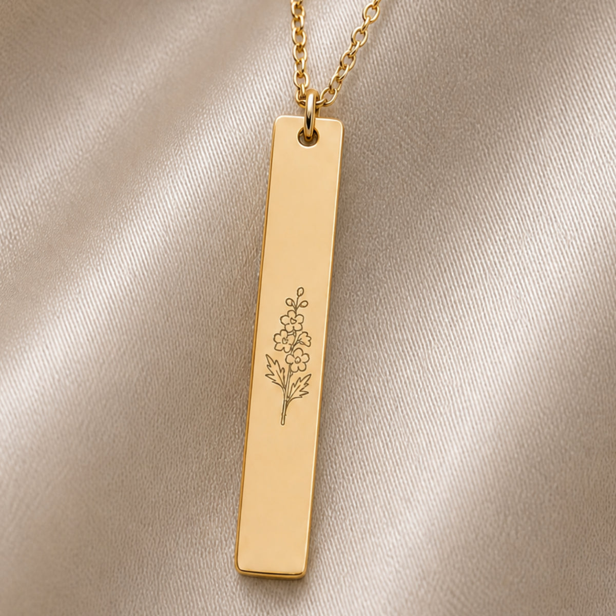 July birth flower necklace — Larkspur engraved vertical bar pendant flatlay with dried botanicals on cream linen