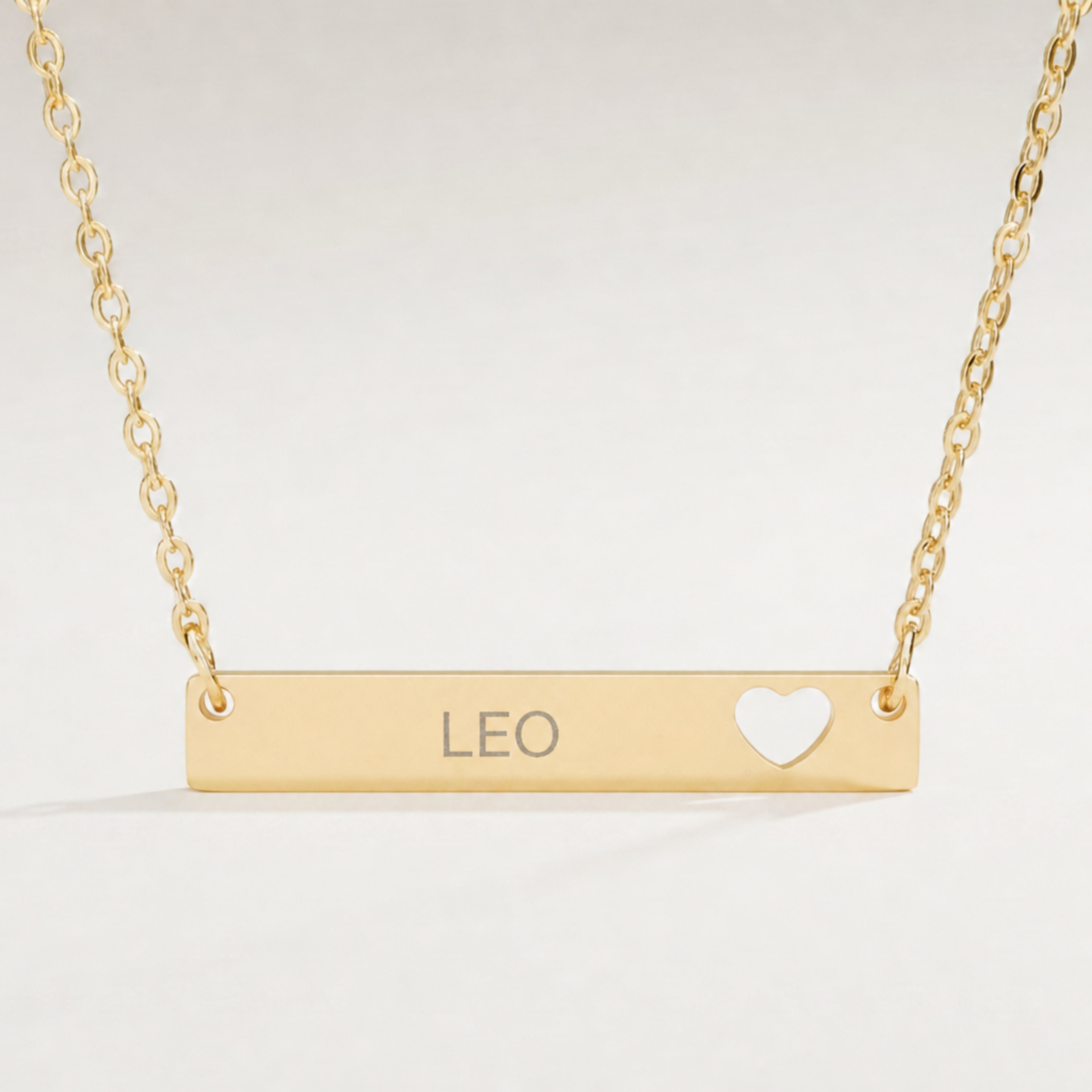 Leo zodiac necklace close-up — 18K Gold polished cutout heart bar pendant with grey laser-etched LEO, see-through heart cutout, premium macro on clean background