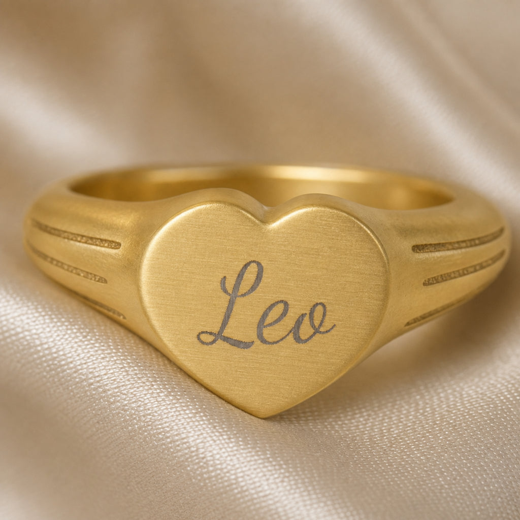 Leo zodiac heart signet ring engraving close-up — laser-etched Leo name detail, brushed grey cursive on matte gold heart