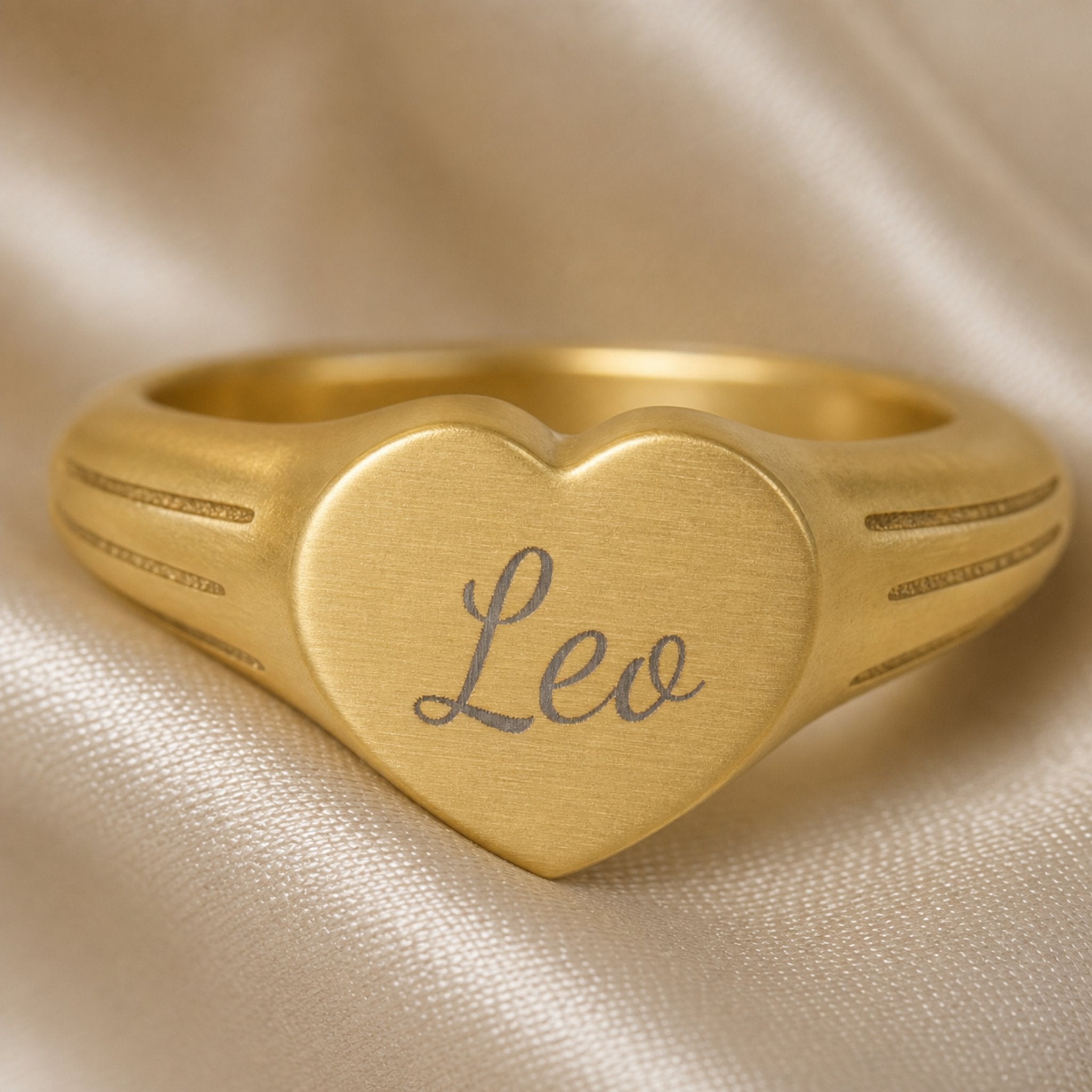 Leo zodiac heart signet ring engraving close-up — laser-etched Leo name detail, brushed grey cursive on matte gold heart