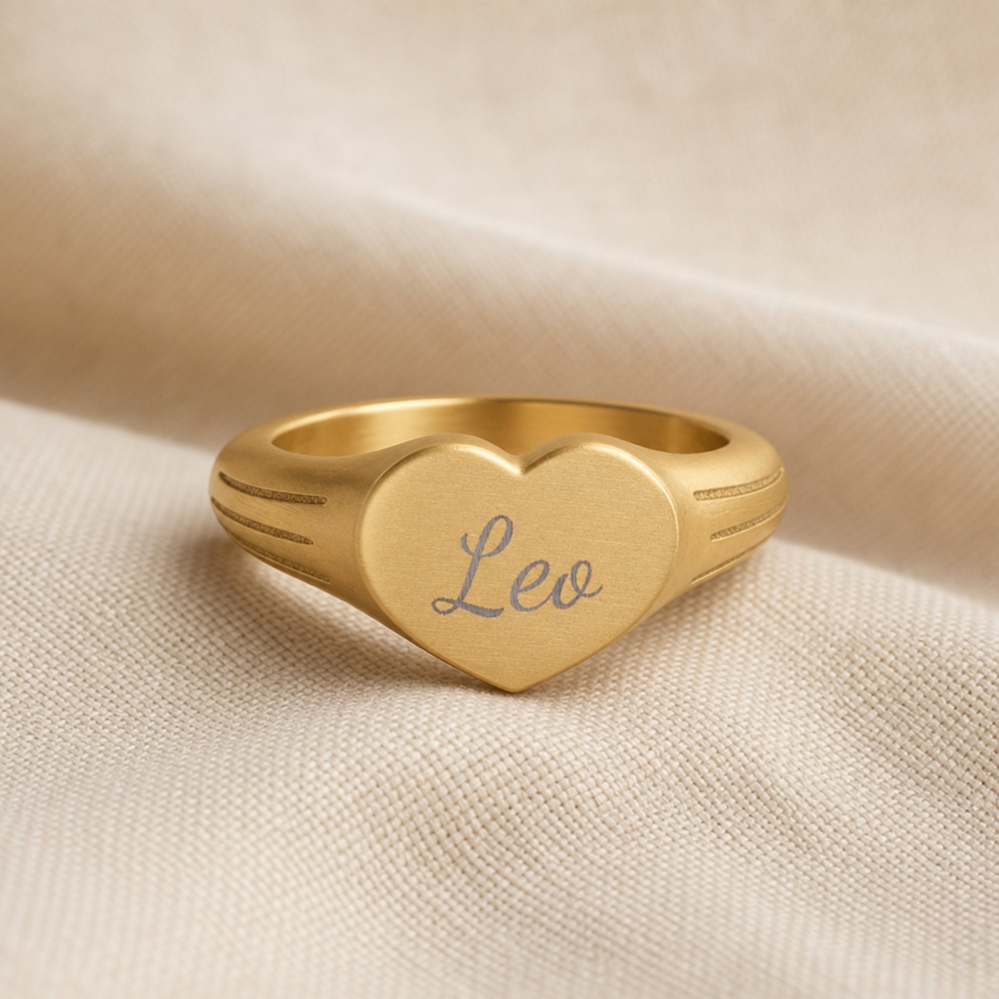 Leo zodiac heart signet ring linen flatlay — engraved Leo heart ring on rumpled cream linen with dried floral, editorial styling