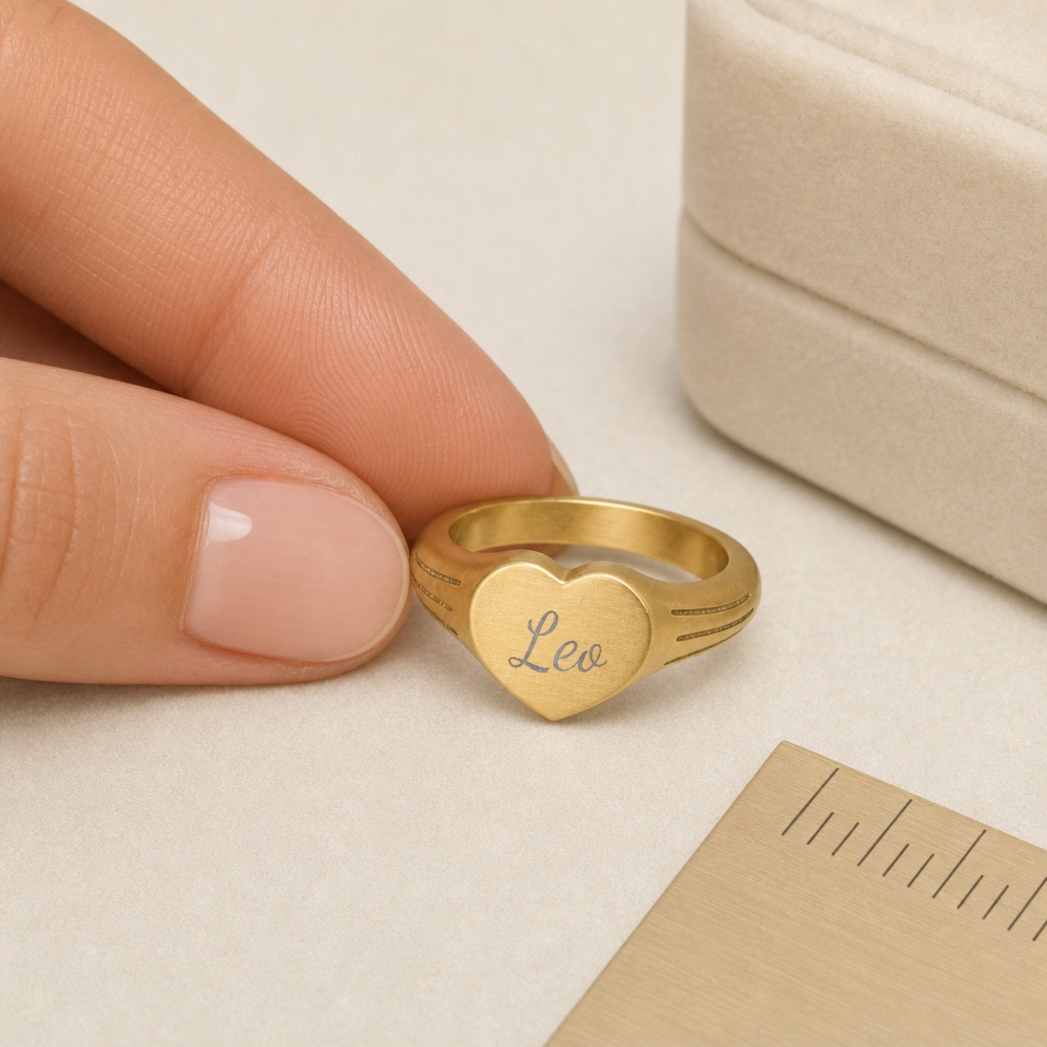 Leo zodiac heart signet ring scale-in-hand — fingers holding heart ring next to gift box and ruler, dainty signet sizing