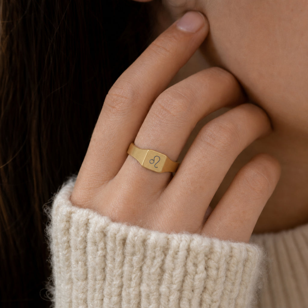 Leo zodiac square signet ring on finger — model wearing engraved Leo signet, cream linen lifestyle moment
