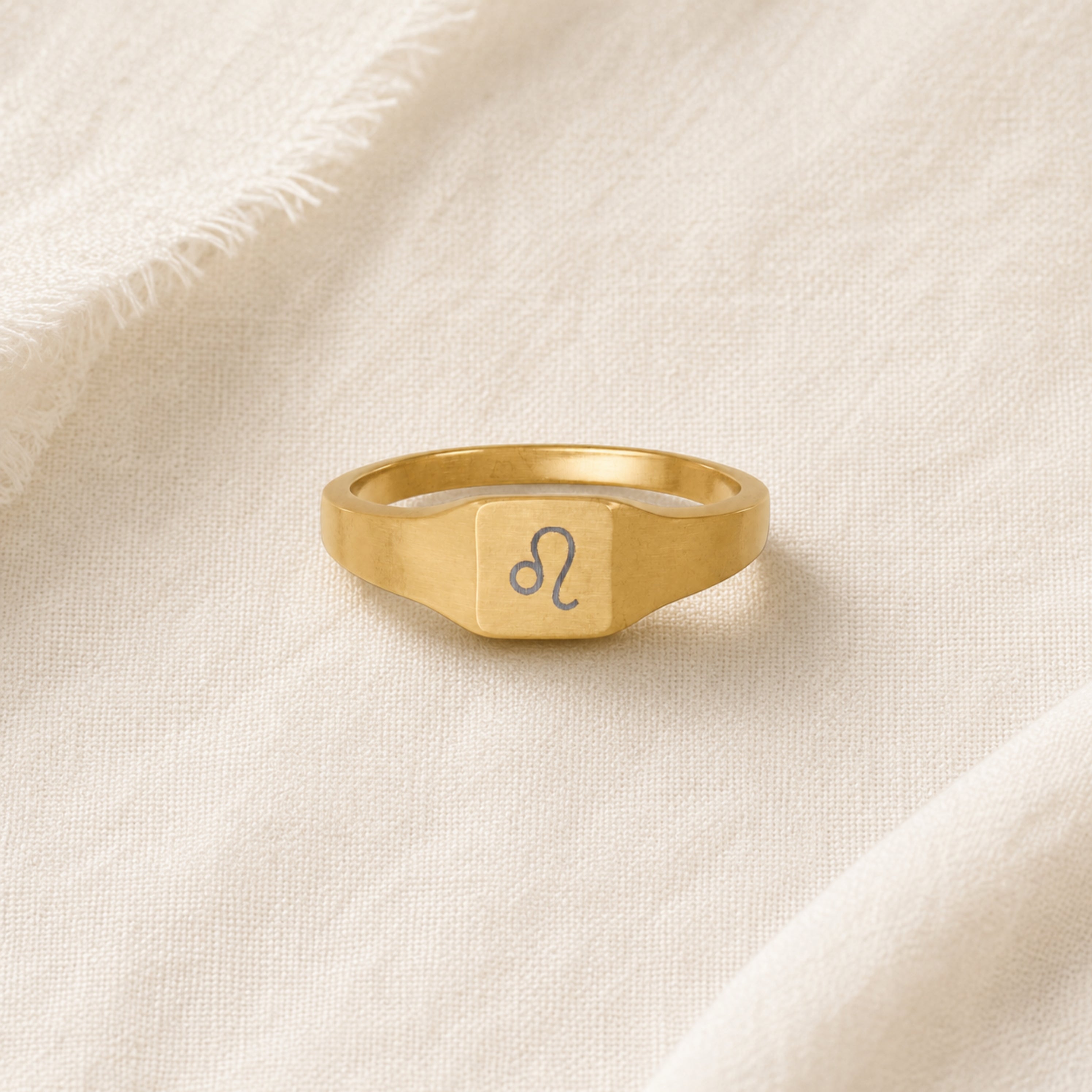 Leo zodiac square signet ring linen flatlay — engraved Lion ring on rumpled cream linen, editorial product shot