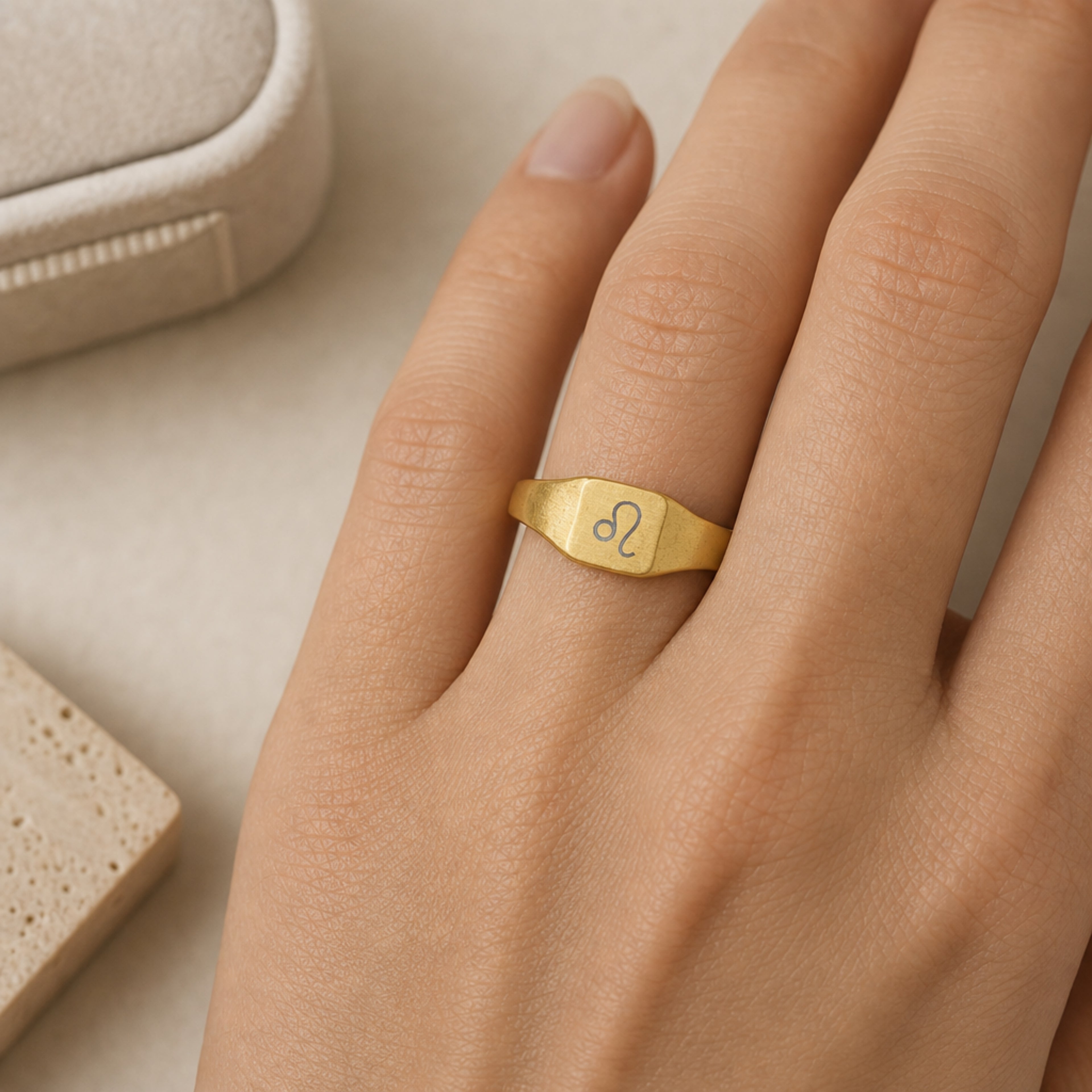 Leo zodiac square signet ring scale-in-hand — fingers holding ring next to gift box and ruler, dainty 20mm signet sizing