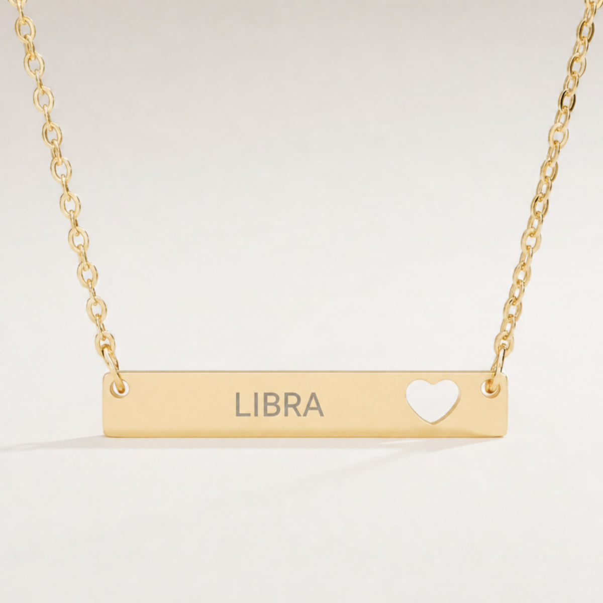 Libra zodiac necklace close-up — 18K Gold polished cutout heart bar pendant with grey laser-etched LIBRA, see-through heart cutout, premium macro on clean background