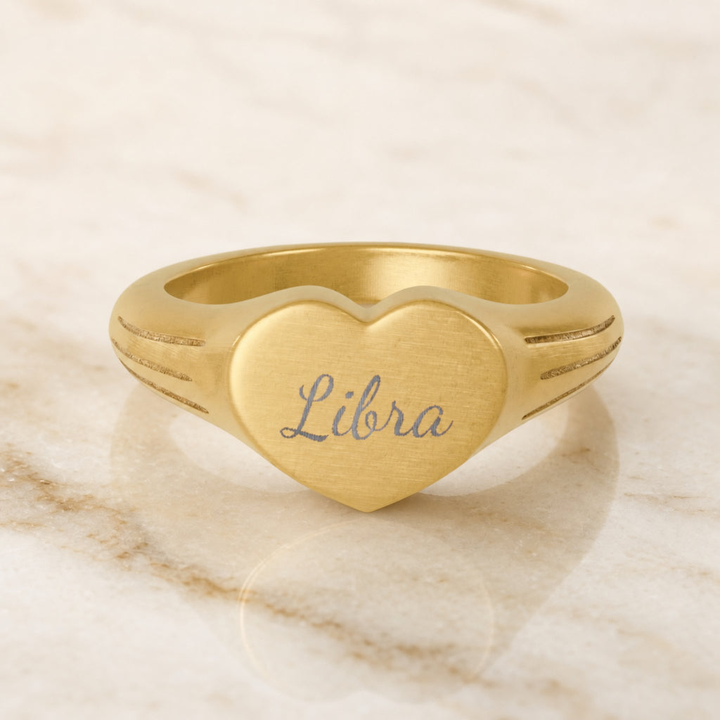 Libra zodiac heart signet ring — hero macro of laser-engraved Libra name in Dancing Script cursive on 18K gold heart face
