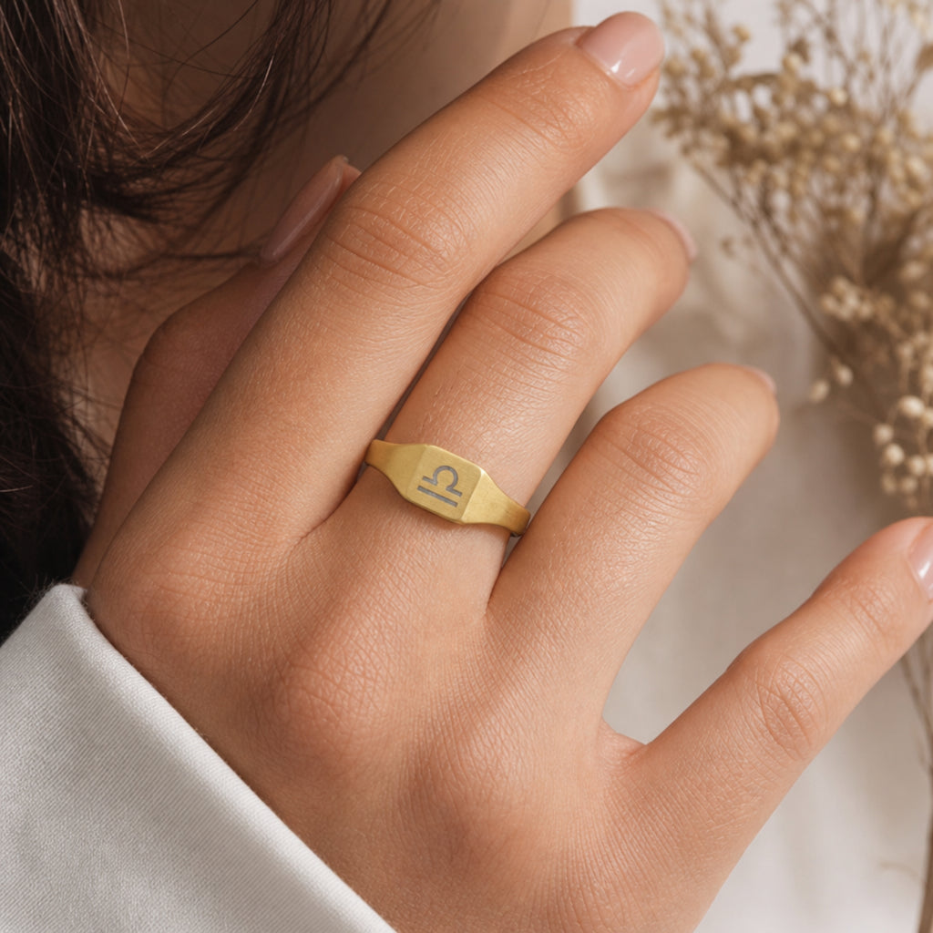Libra zodiac square signet ring on finger — model wearing engraved Libra signet, cream linen lifestyle moment