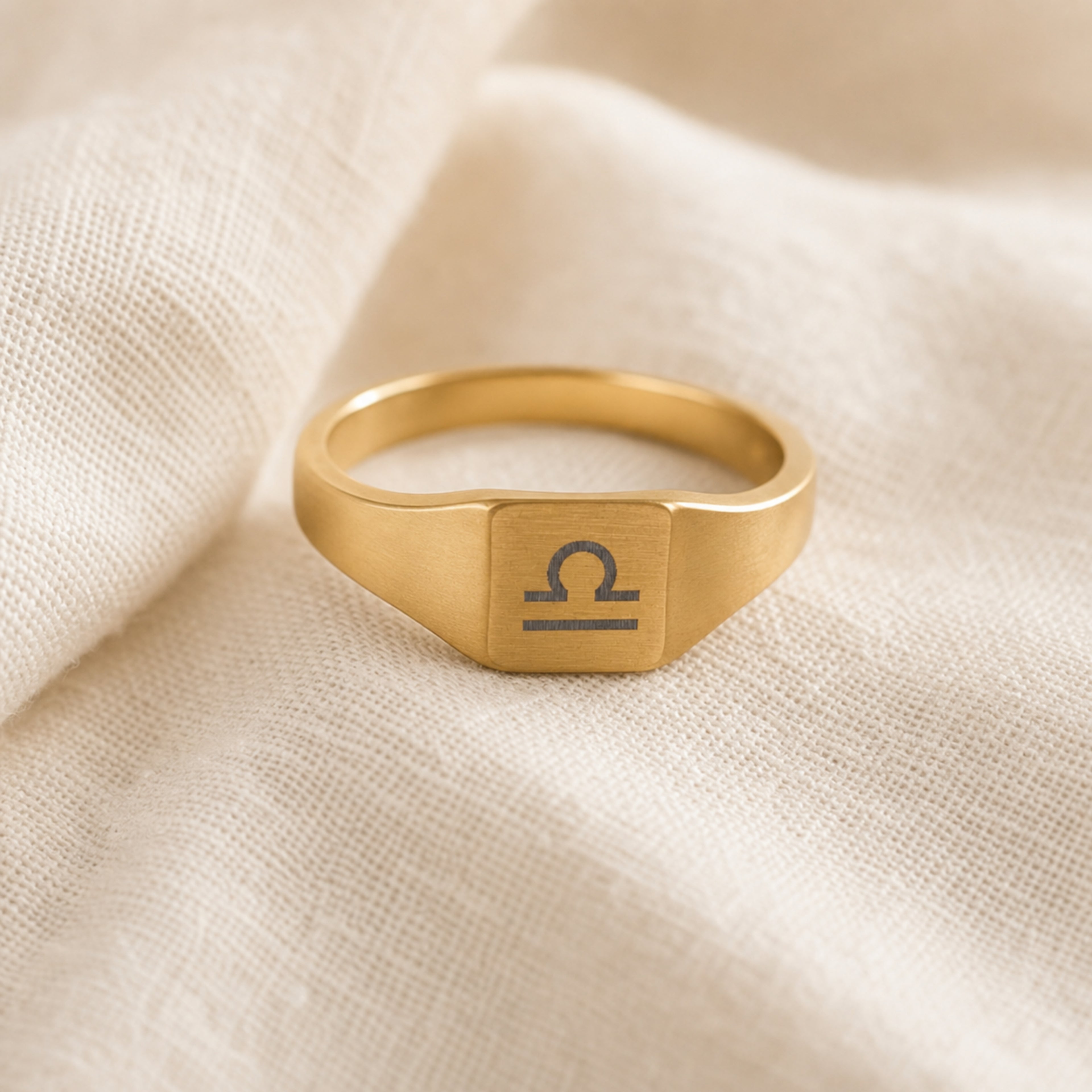 Libra zodiac square signet ring linen flatlay — engraved Scales ring on rumpled cream linen, editorial product shot