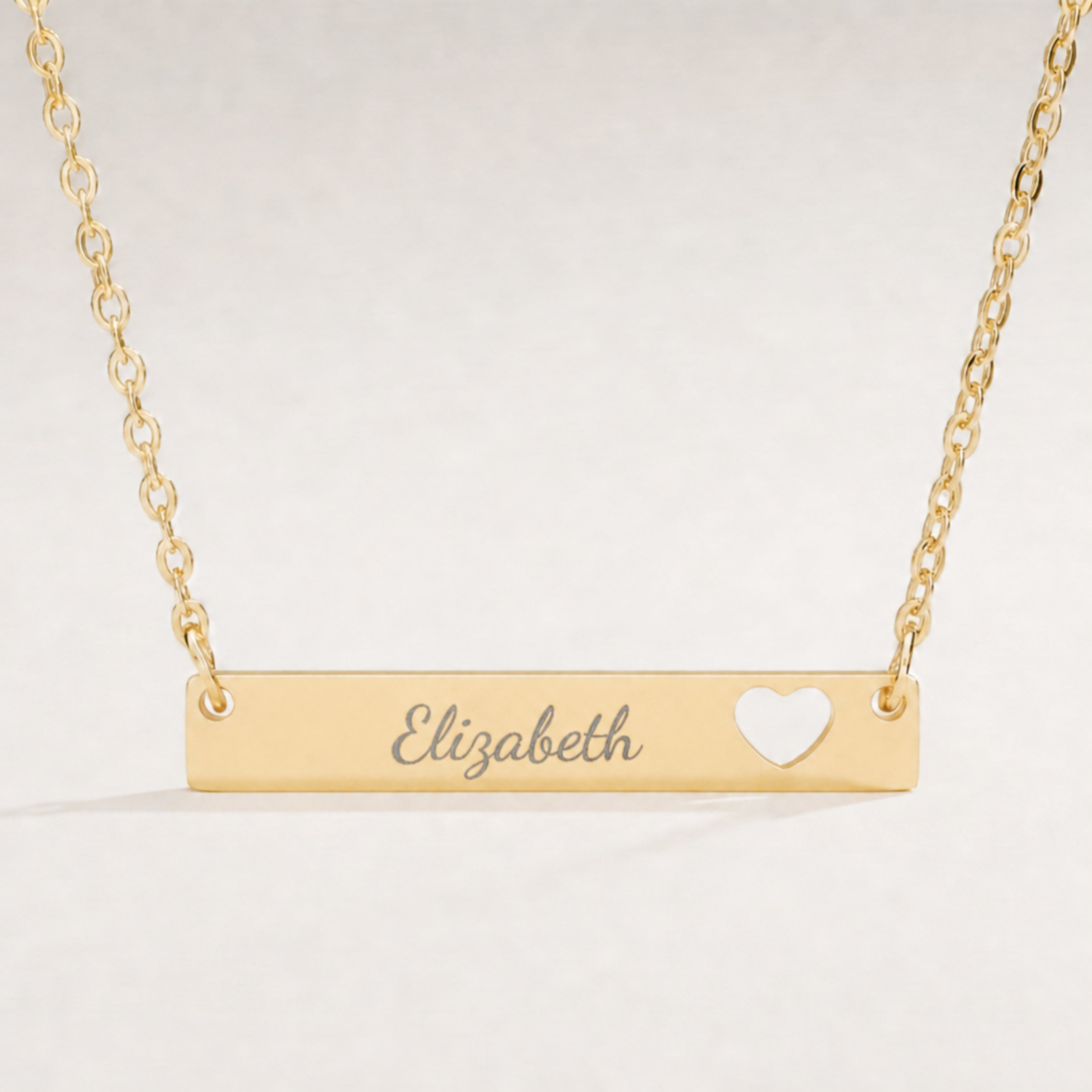 Close-up of the engraved name on a gold heart-cutout bar pendant