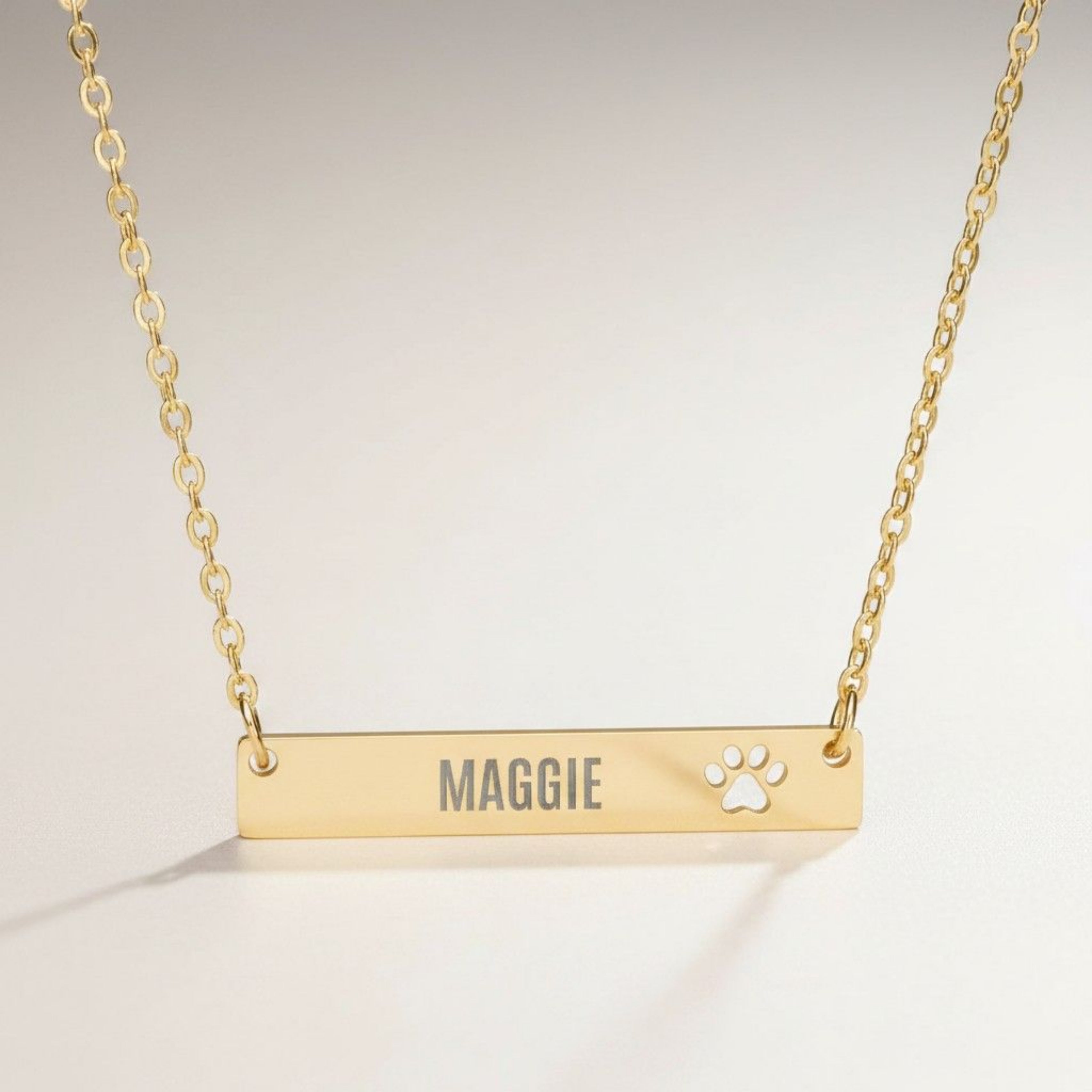 Close-up of the engraved name and cutout paw on a gold pet name bar pendant