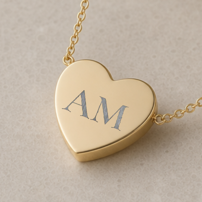 Personalized engraved initial heart necklace in 18K gold, an open heart beside a small initial charm, flat lay on linen