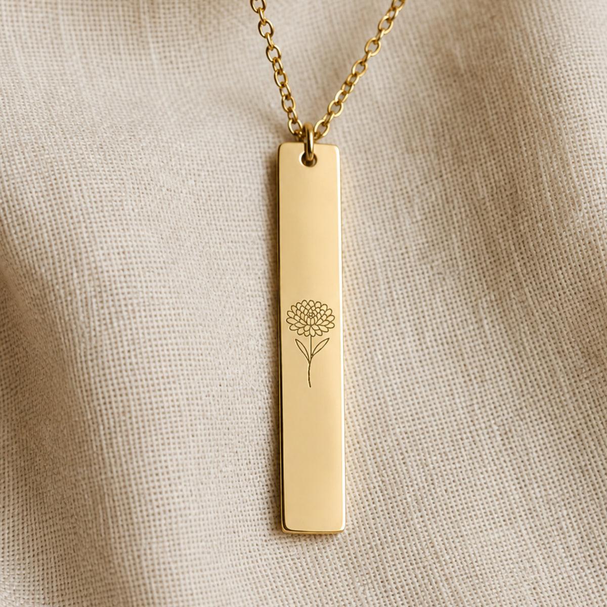 November birth flower necklace — Chrysanthemum engraved vertical bar pendant flatlay with dried botanicals on cream linen