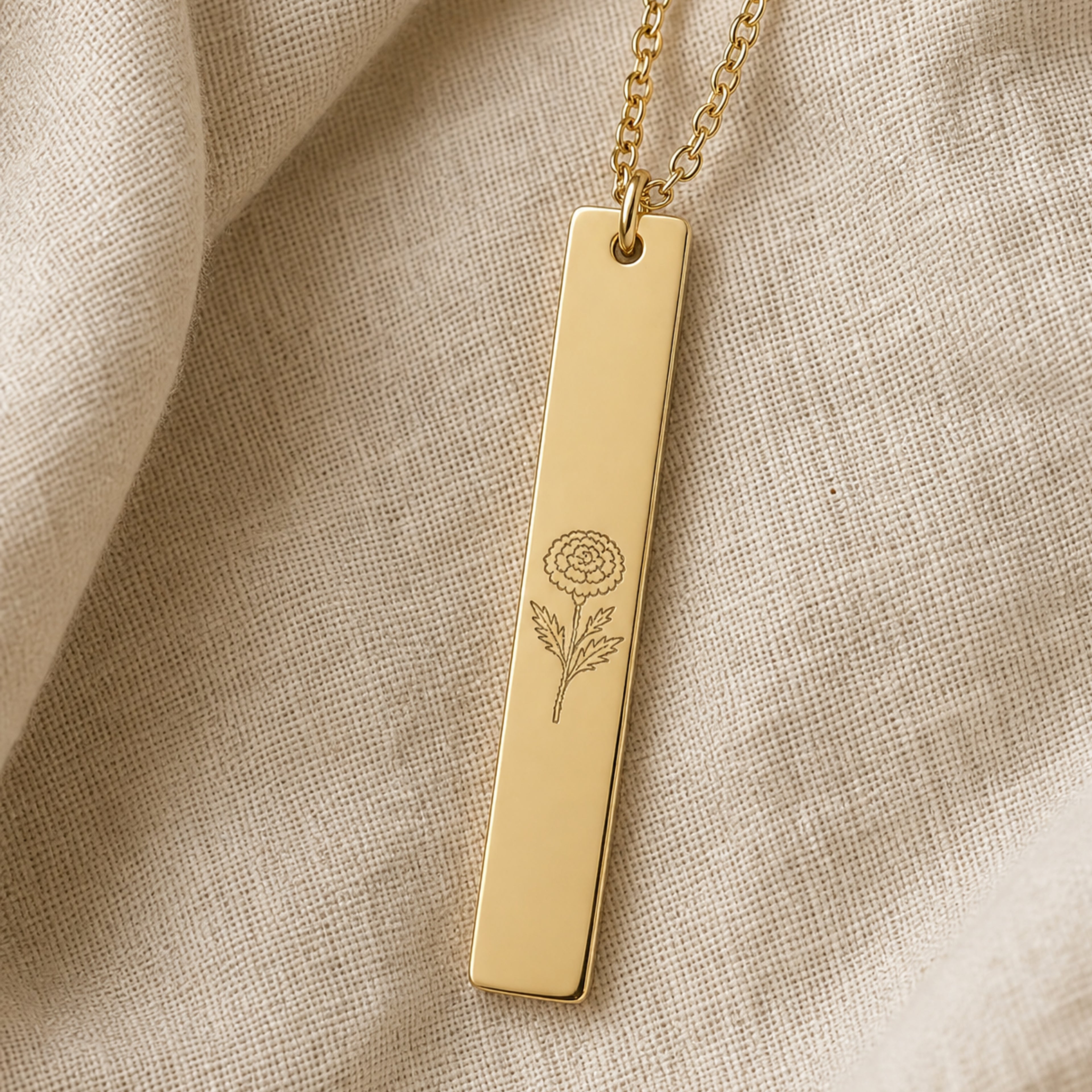 October birth flower necklace — Marigold engraved vertical bar pendant flatlay with dried botanicals on cream linen