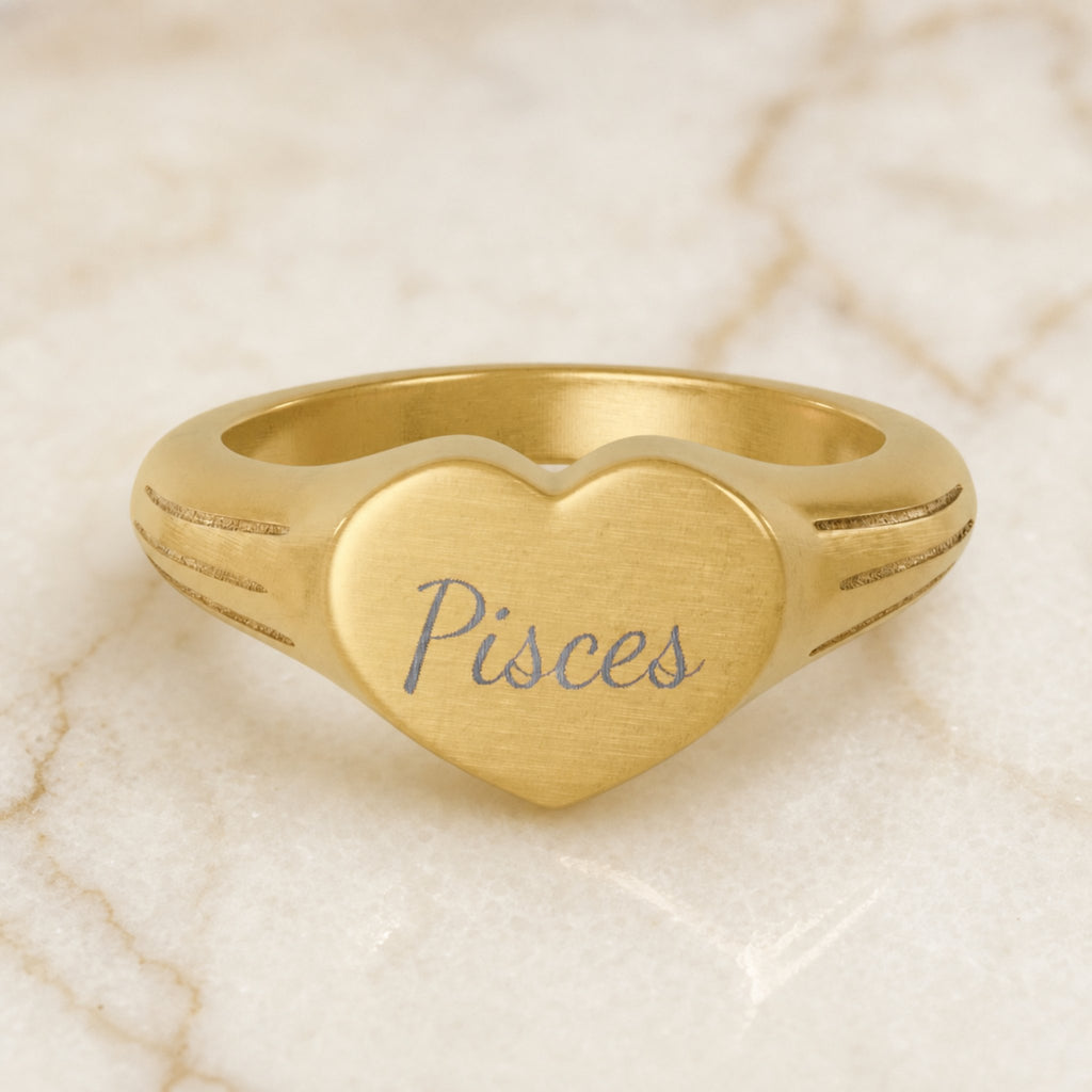 Pisces zodiac heart signet ring — hero macro of laser-engraved Pisces name in Dancing Script cursive on 18K gold heart face
