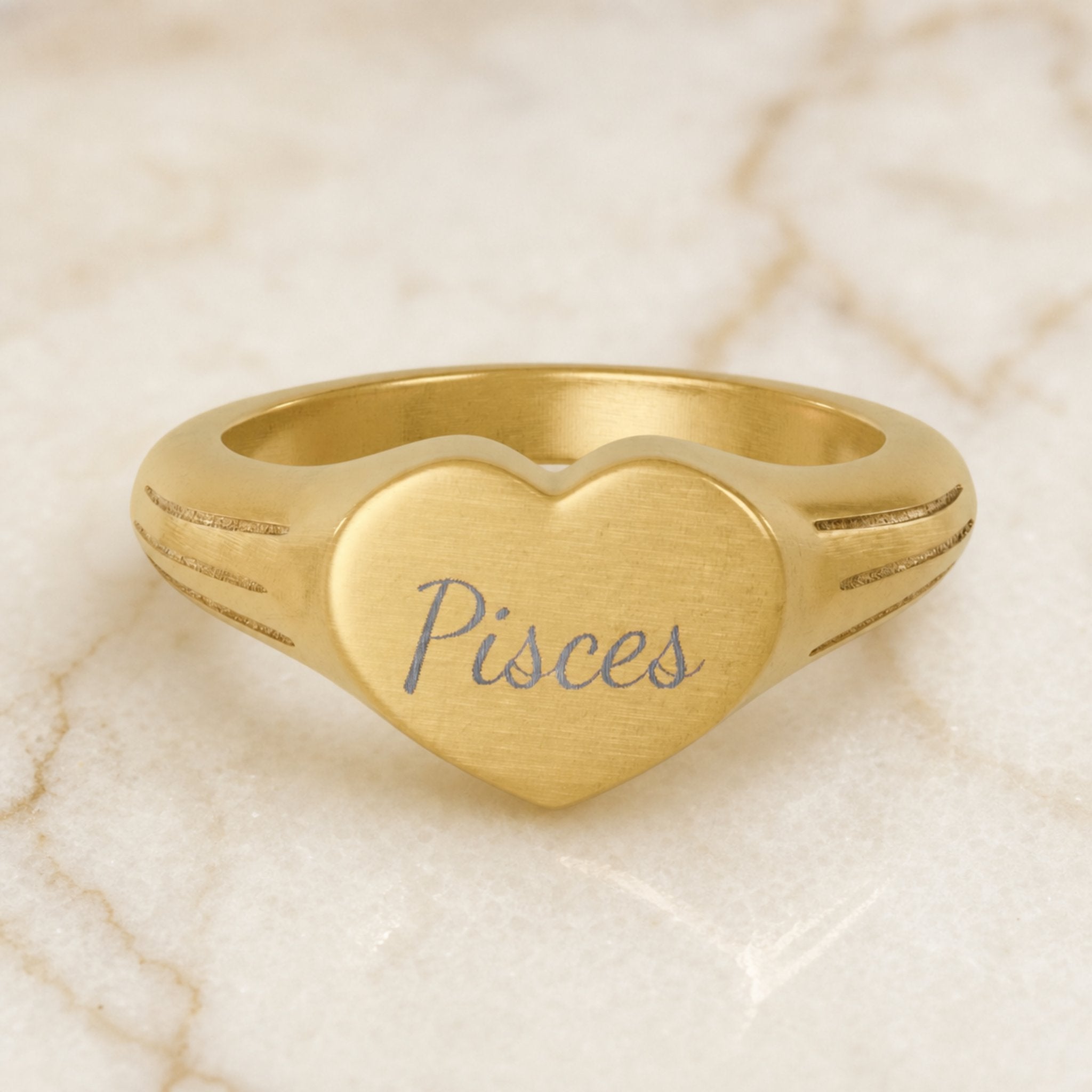 Pisces zodiac heart signet ring — hero macro of laser-engraved Pisces name in Dancing Script cursive on 18K gold heart face
