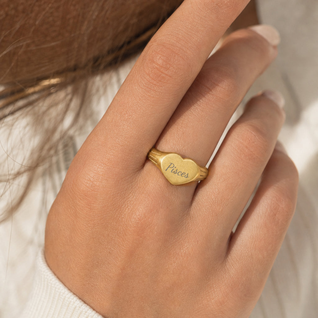 Pisces zodiac heart signet ring on finger — model wearing engraved Pisces heart signet, cream linen lifestyle moment
