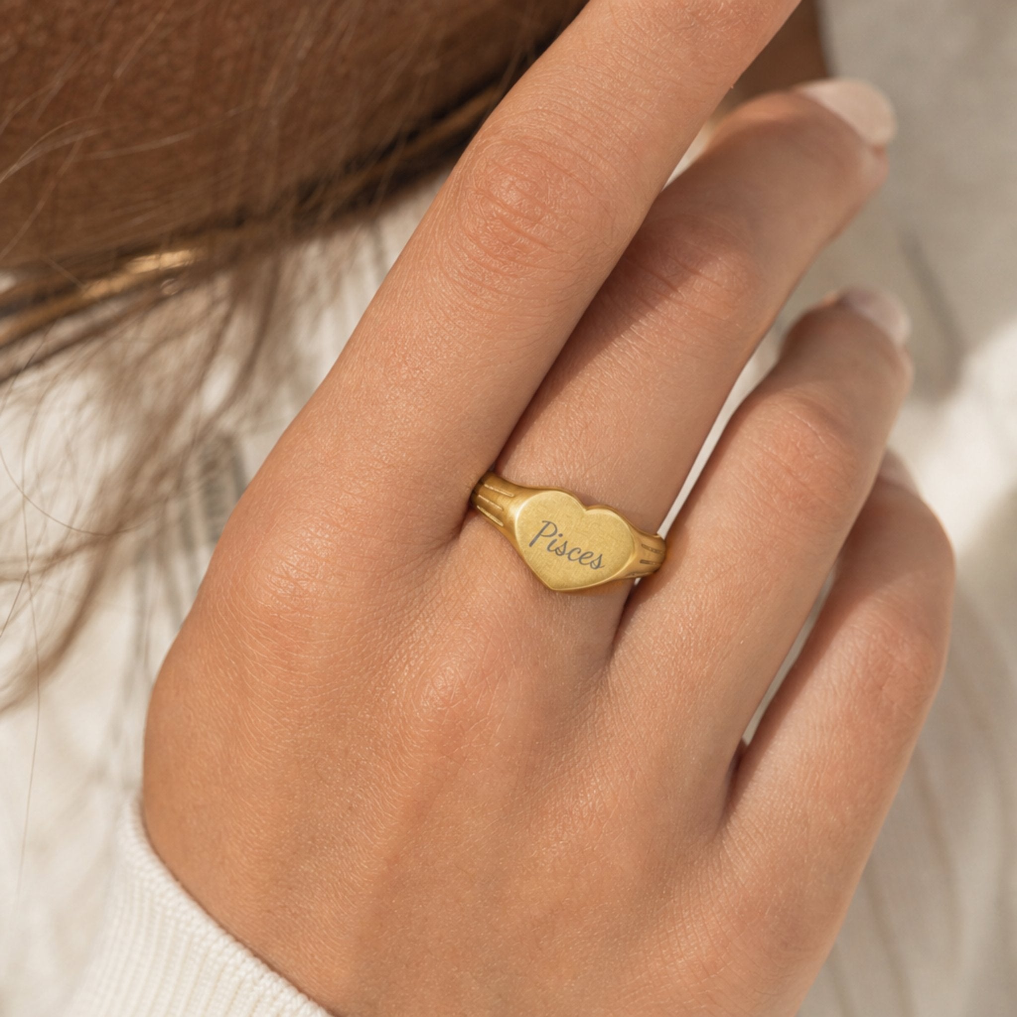 Pisces zodiac heart signet ring on finger — model wearing engraved Pisces heart signet, cream linen lifestyle moment