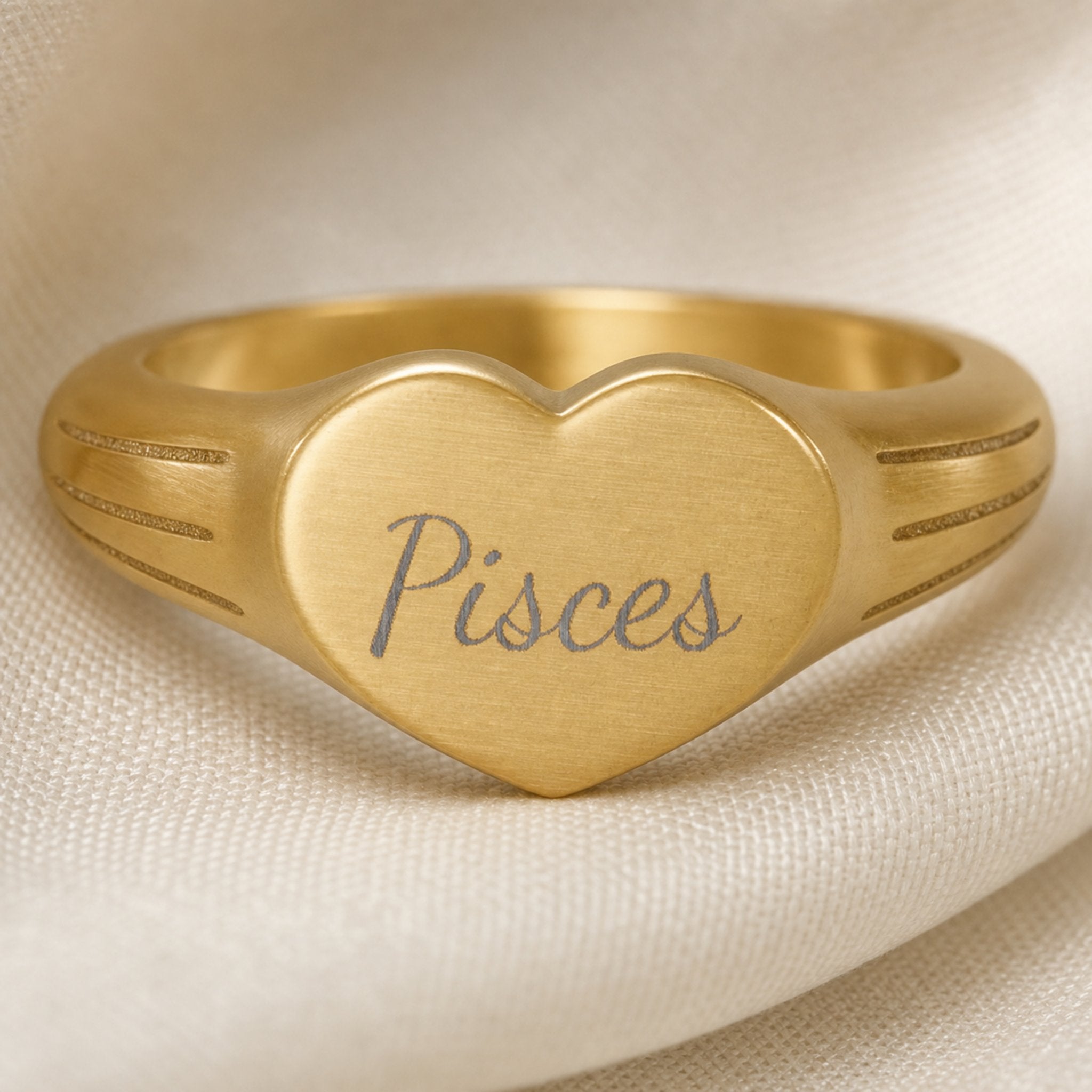 Pisces zodiac heart signet ring engraving close-up — laser-etched Pisces name detail, brushed grey cursive on matte gold heart