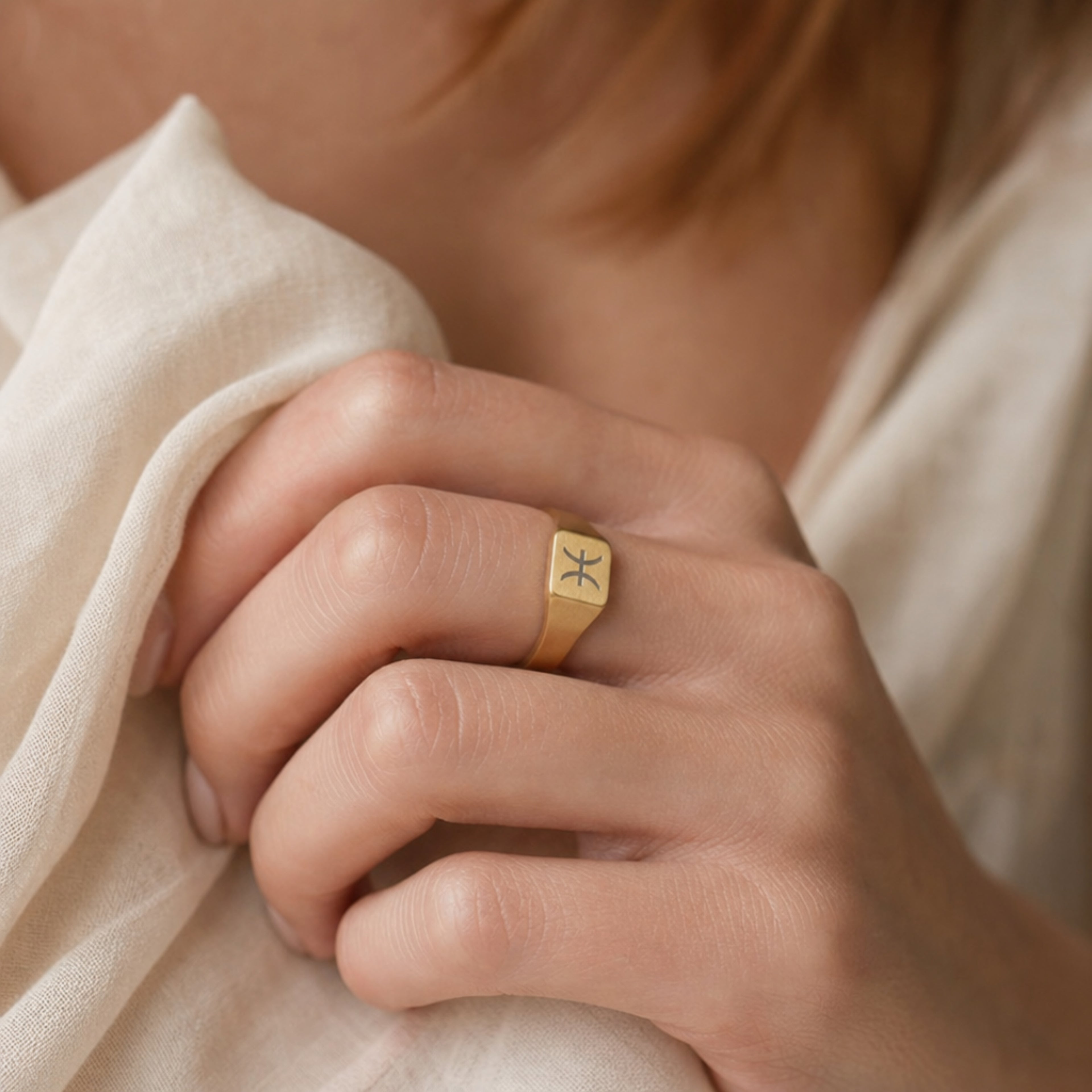 Pisces zodiac square signet ring on finger — model wearing engraved Pisces signet, cream linen lifestyle moment