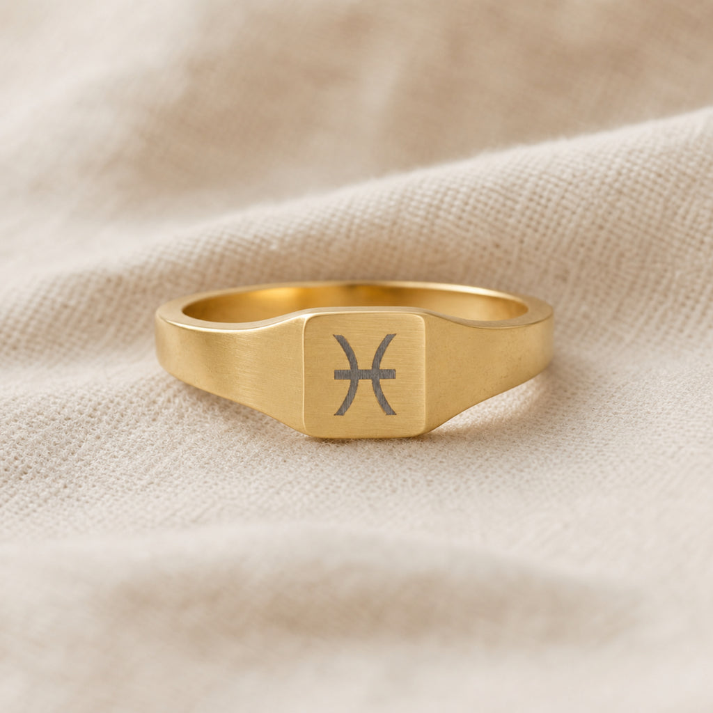 Pisces zodiac square signet ring linen flatlay — engraved Pisces ring on rumpled cream linen, editorial product shot