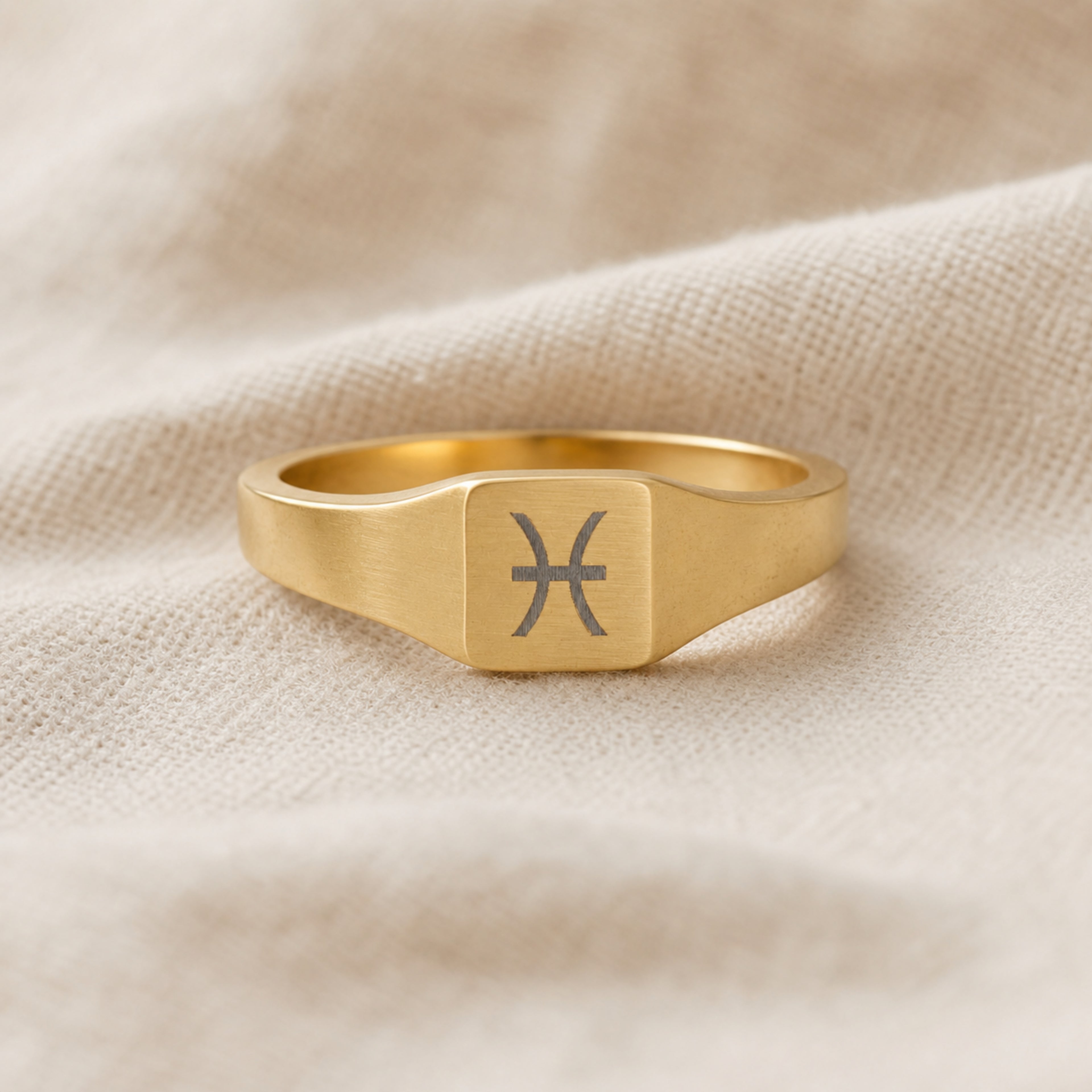 Pisces zodiac square signet ring linen flatlay — engraved Pisces ring on rumpled cream linen, editorial product shot
