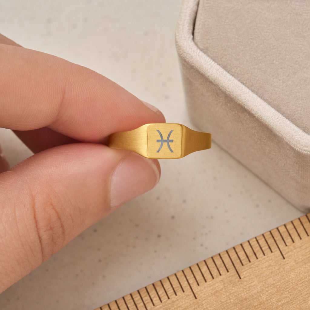 Pisces zodiac square signet ring scale-in-hand — fingers holding ring next to gift box and ruler, dainty 20mm signet sizing