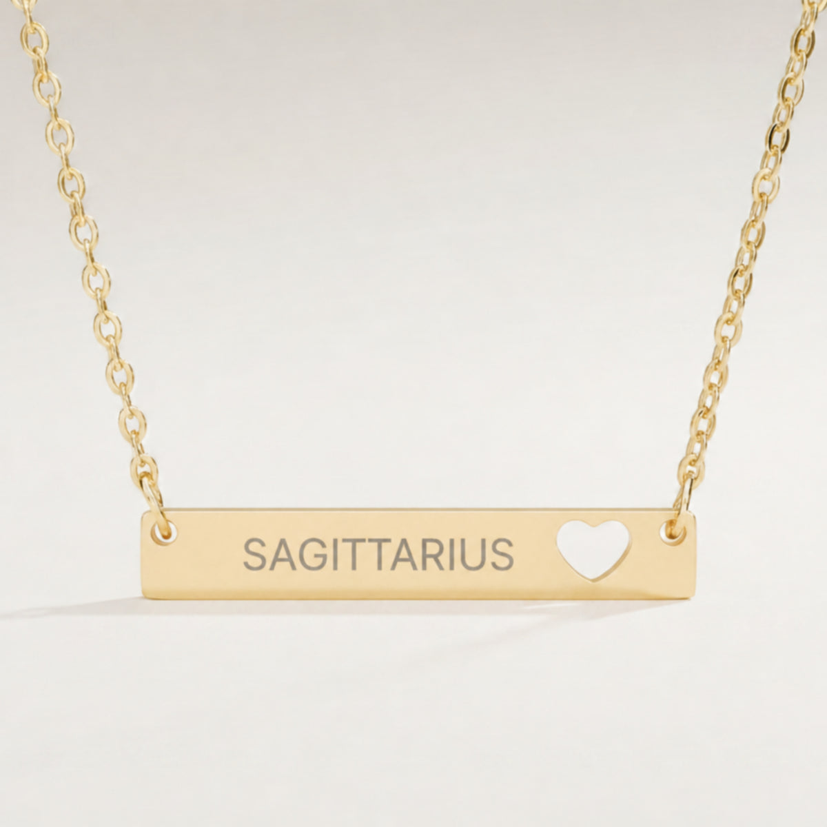 Sagittarius zodiac necklace close-up — 18K Gold polished cutout heart bar pendant with grey laser-etched SAGITTARIUS, see-through heart cutout, premium macro on clean background