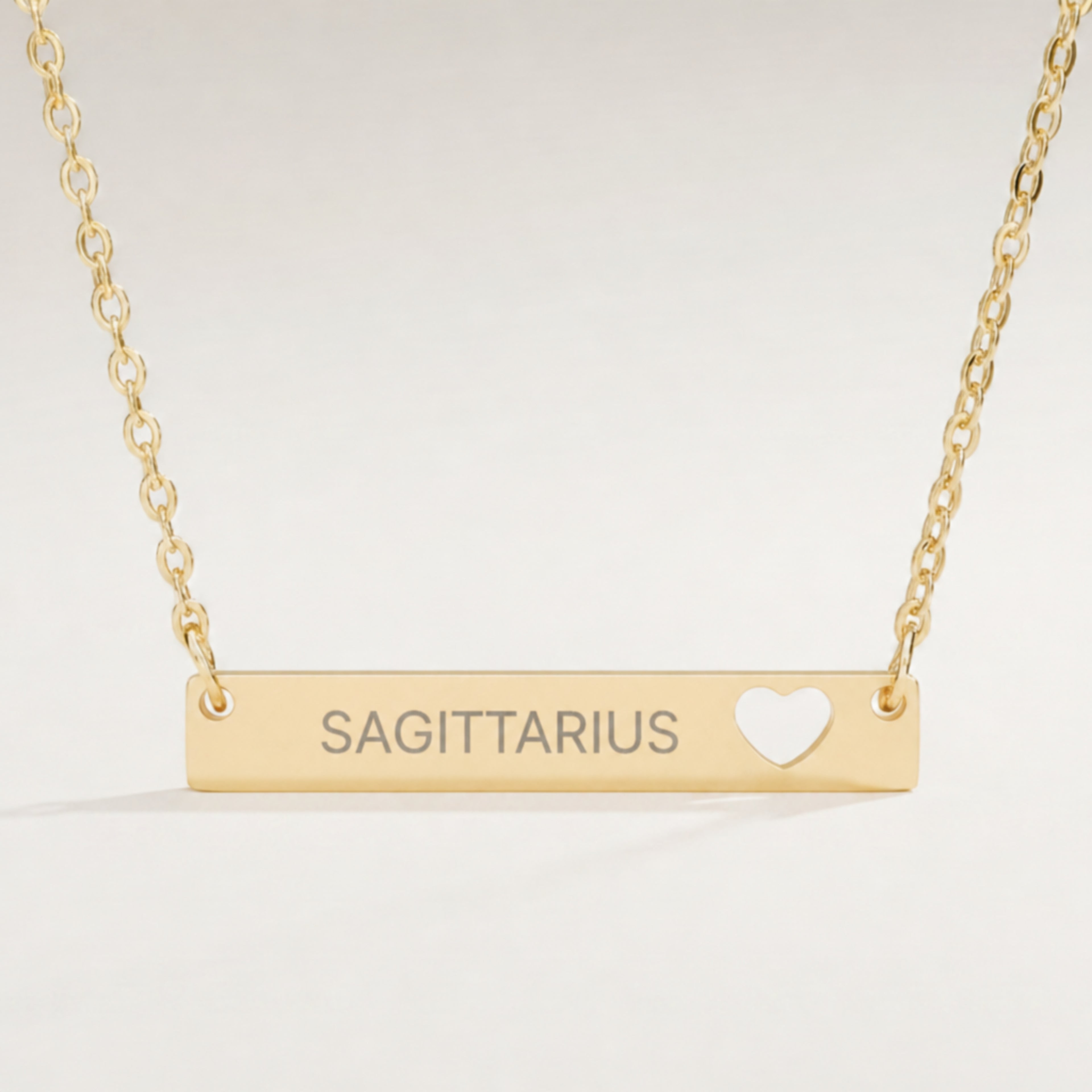 Sagittarius zodiac necklace close-up — 18K Gold polished cutout heart bar pendant with grey laser-etched SAGITTARIUS, see-through heart cutout, premium macro on clean background