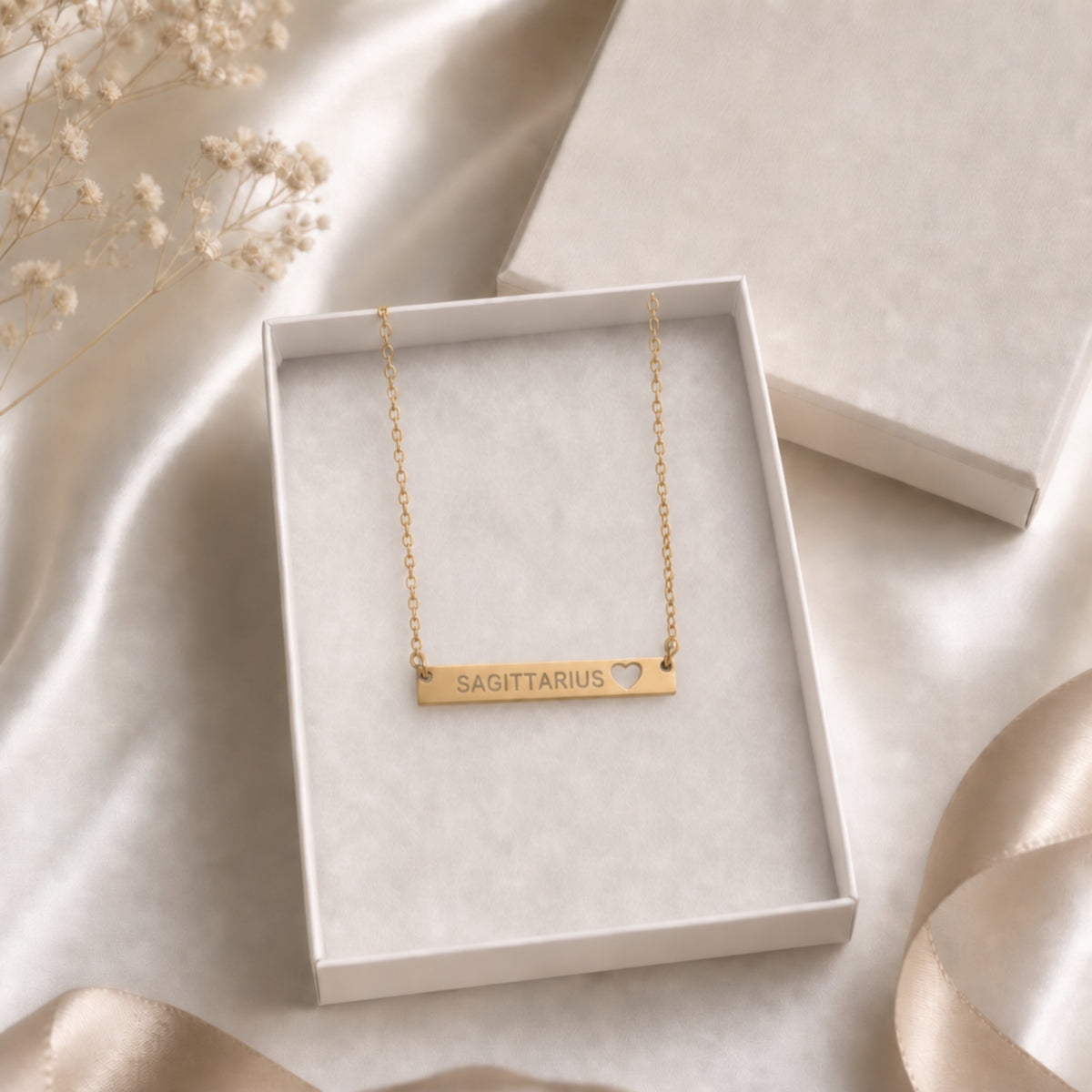 The Sagittarius zodiac necklace nestled in Memory That Lasts signature cream gift box — 18K Gold cutout heart bar pendant with grey laser-etched SAGITTARIUS, satin lining, premium unboxing moment