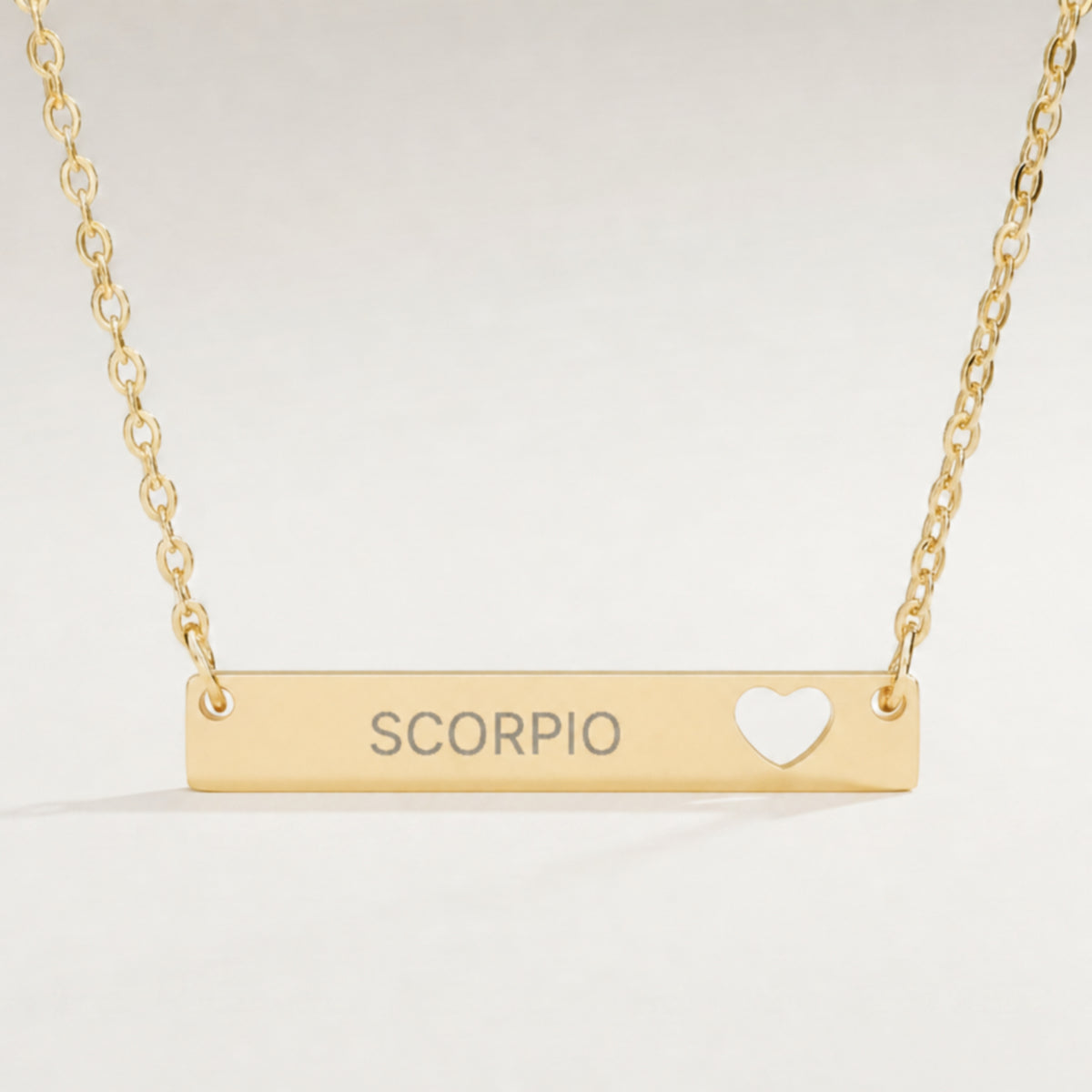 Scorpio zodiac necklace close-up — 18K Gold polished cutout heart bar pendant with grey laser-etched SCORPIO, see-through heart cutout, premium macro on clean background