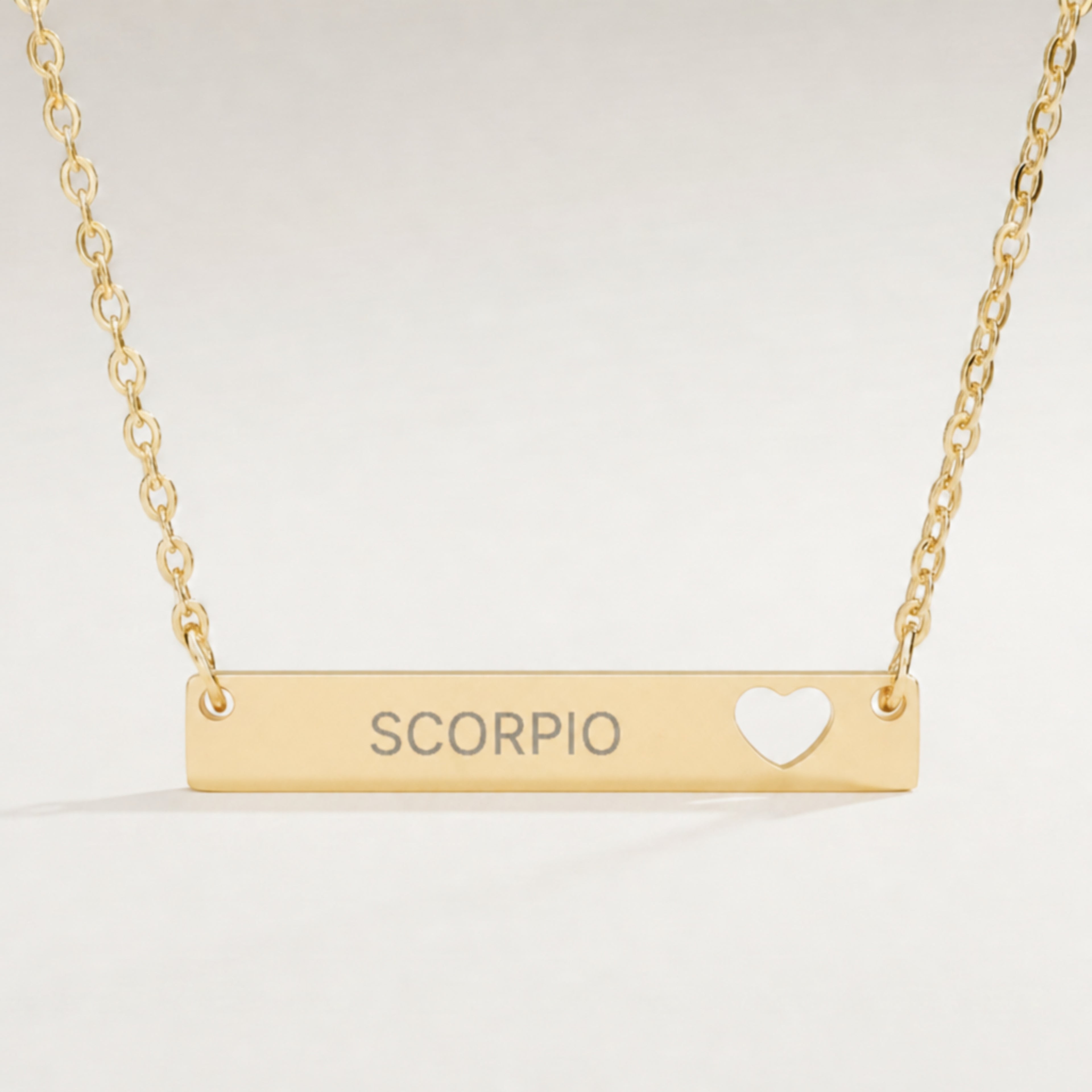 Scorpio zodiac necklace close-up — 18K Gold polished cutout heart bar pendant with grey laser-etched SCORPIO, see-through heart cutout, premium macro on clean background