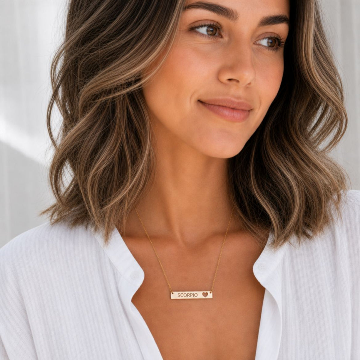 Model wearing the Scorpio zodiac necklace in 18K Gold — polished cutout heart bar with grey laser-etched SCORPIO, see-through heart cutout shows skin tone, white blouse, soft natural daylight