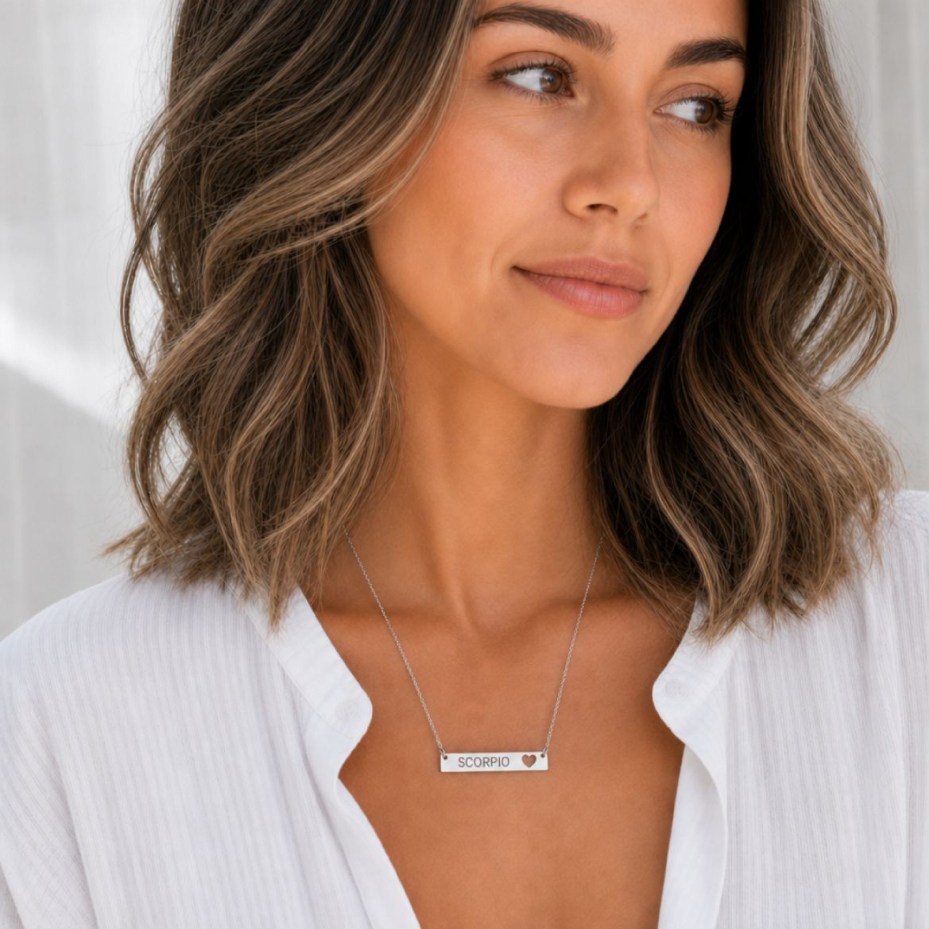 Model wearing the Scorpio zodiac necklace in 316L stainless steel — polished mirror cutout heart bar with grey laser-etched SCORPIO, see-through heart cutout, white blouse, soft natural daylight