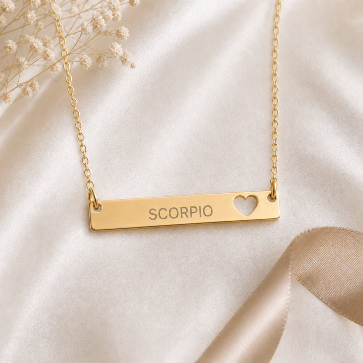 Cream-linen flat lay of the Scorpio zodiac necklace — 18K Gold cutout heart bar pendant with grey laser-etched SCORPIO, dried baby's breath, editorial styling