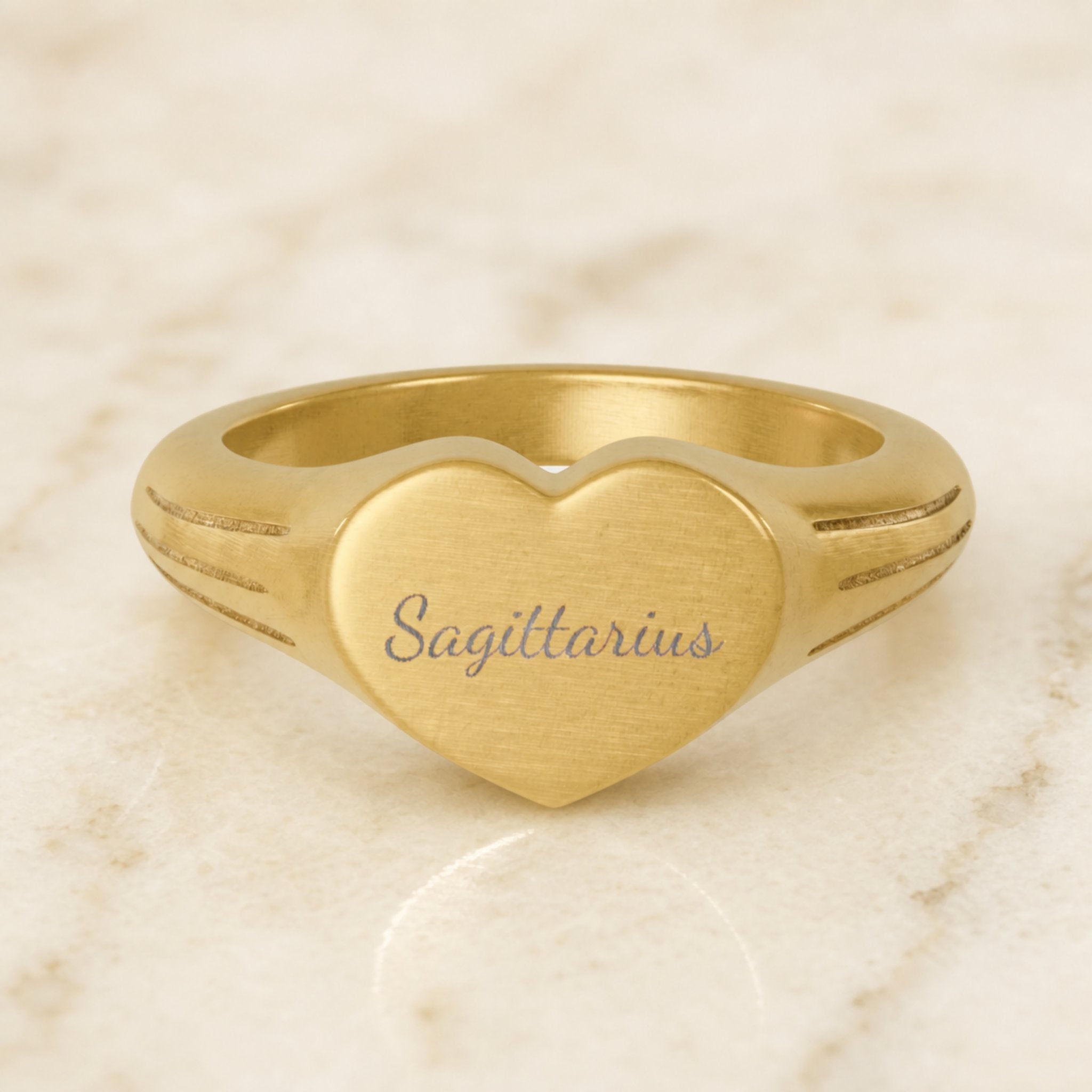 Sagittarius zodiac heart signet ring — hero macro of laser-engraved Sagittarius name in Dancing Script cursive on 18K gold heart face