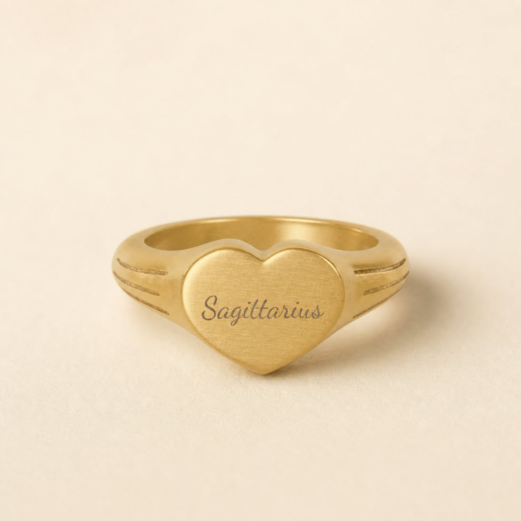 Sagittarius zodiac heart signet ring studio front — clean cream backdrop product shot, 18K gold matte PVD