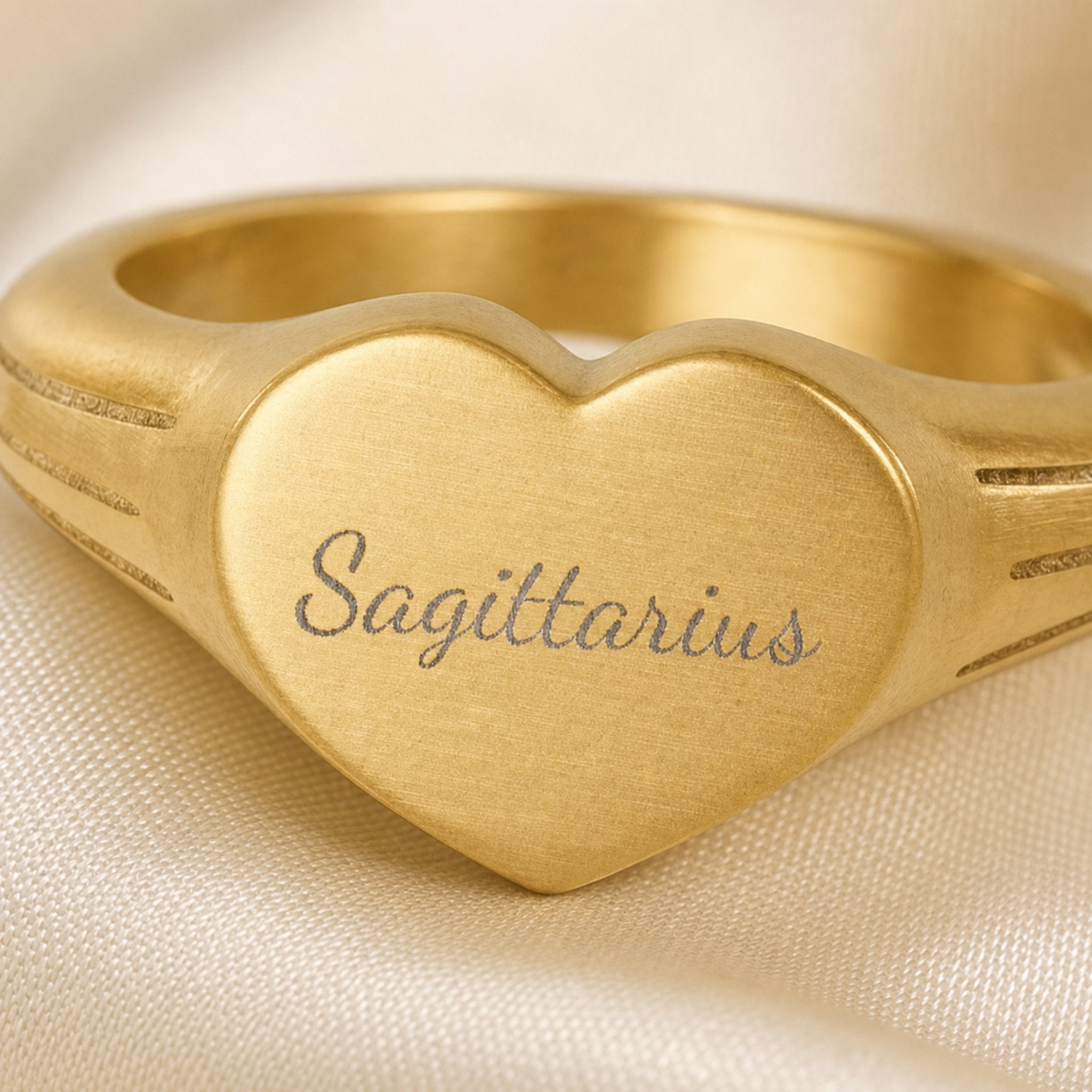 Sagittarius zodiac heart signet ring engraving close-up — laser-etched Sagittarius name detail, brushed grey cursive on matte gold heart