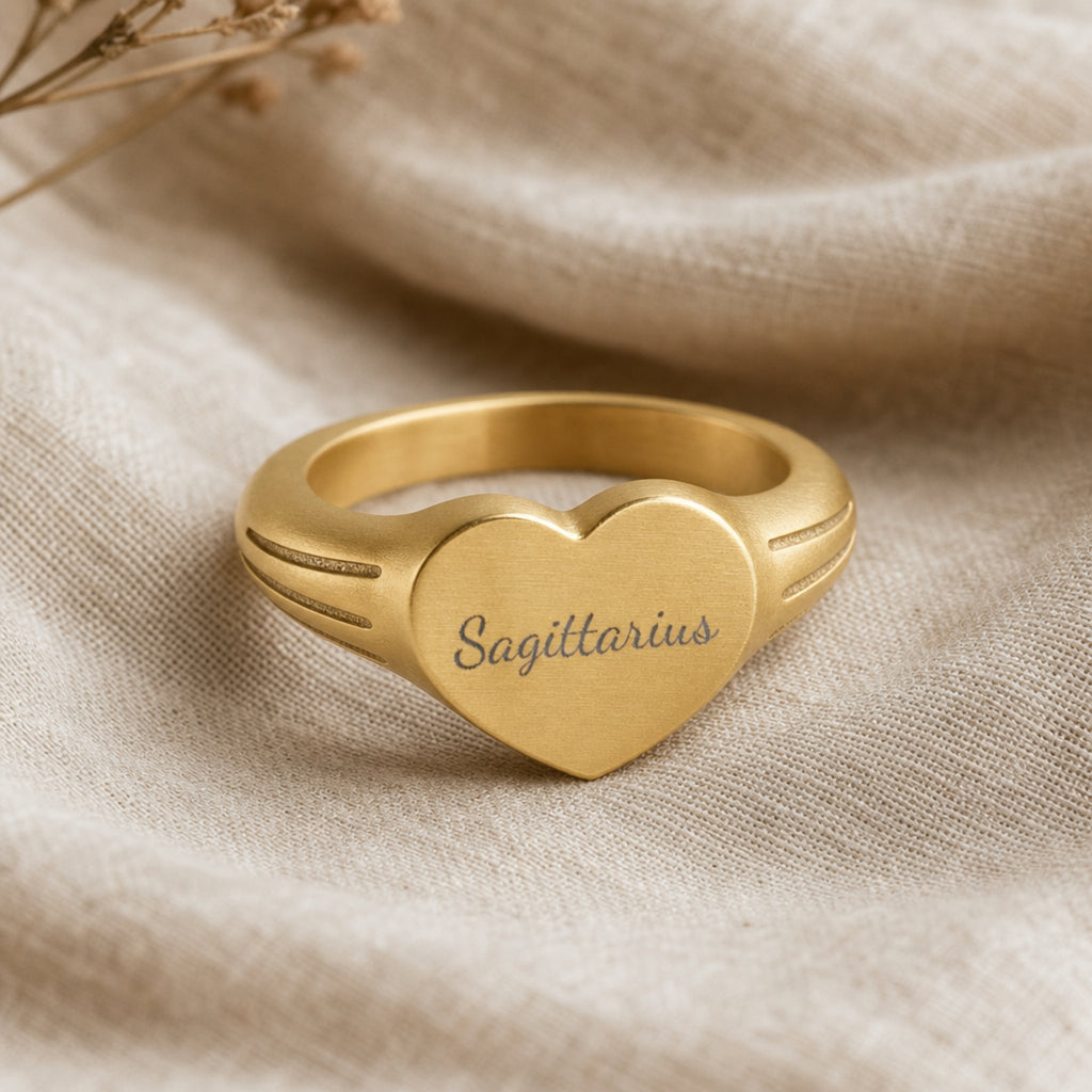 Sagittarius zodiac heart signet ring linen flatlay — engraved Sagittarius heart ring on rumpled cream linen with dried floral, editorial styling