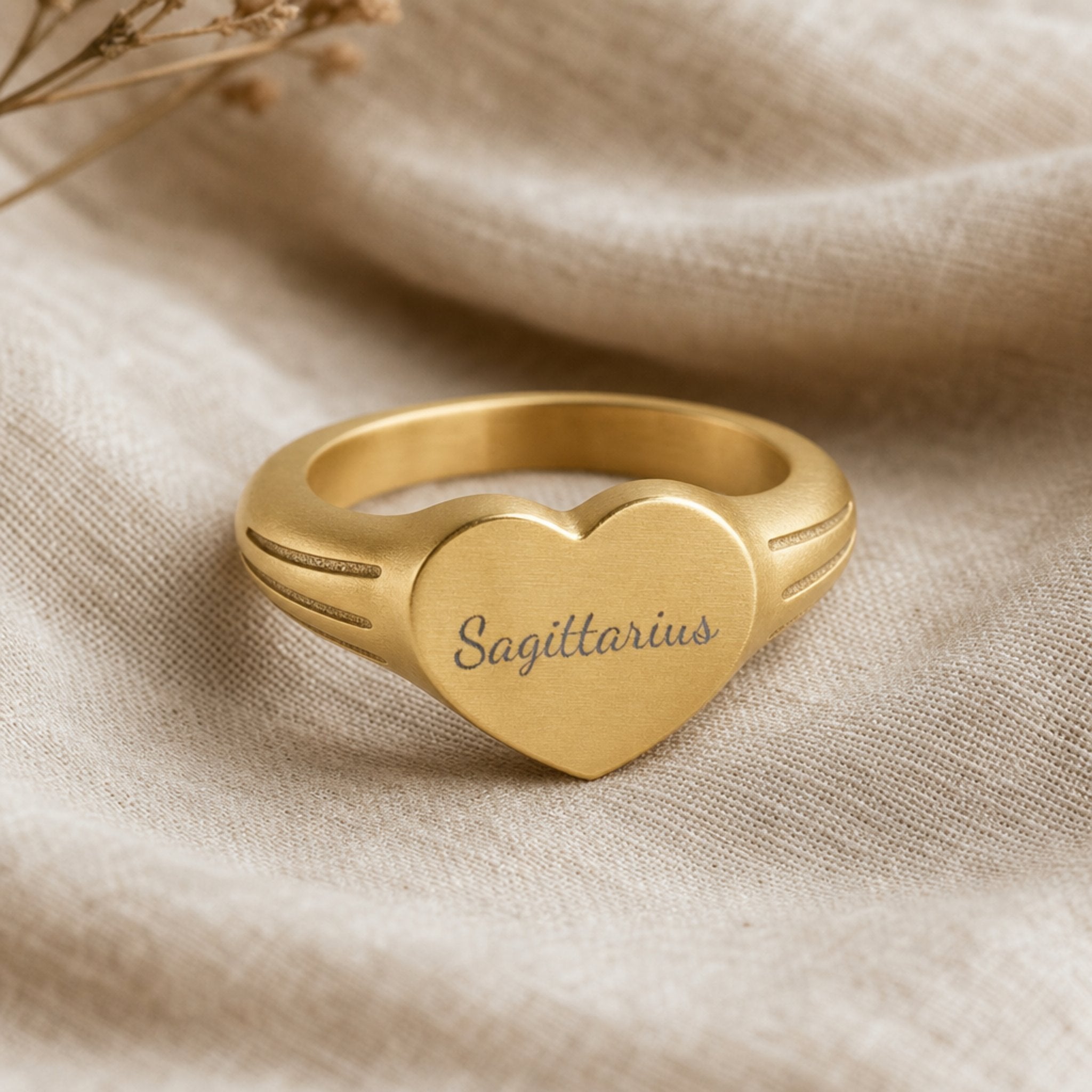 Sagittarius zodiac heart signet ring linen flatlay — engraved Sagittarius heart ring on rumpled cream linen with dried floral, editorial styling