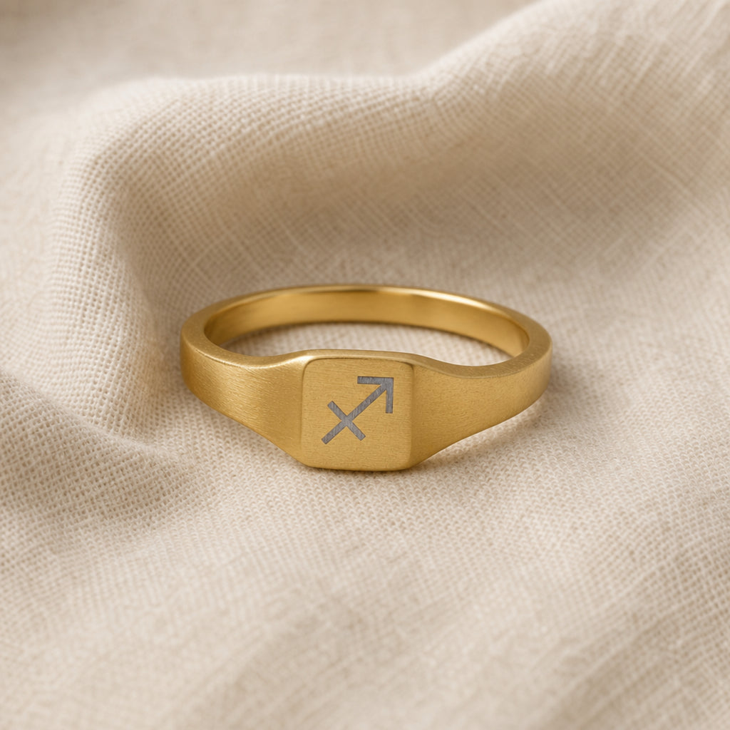 Sagittarius zodiac square signet ring linen flatlay — engraved Archer ring on rumpled cream linen, editorial product shot