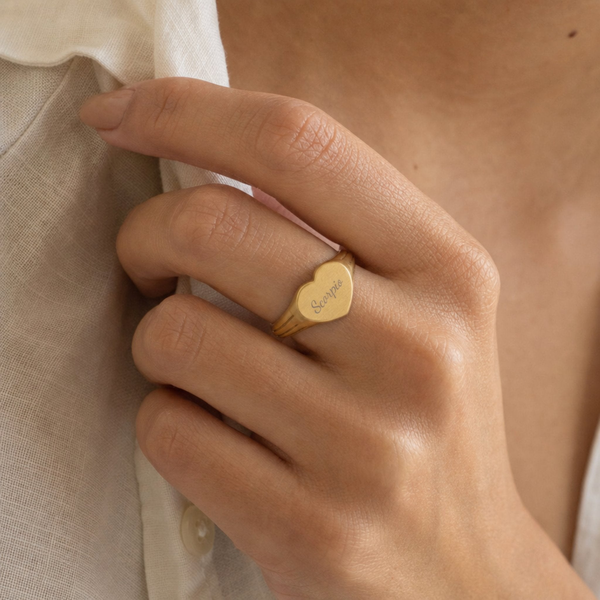Scorpio zodiac heart signet ring on finger — model wearing engraved Scorpio heart signet, cream linen lifestyle moment