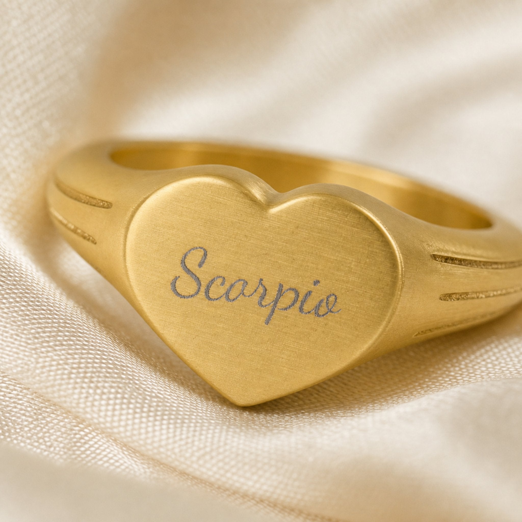 Scorpio zodiac heart signet ring engraving close-up — laser-etched Scorpio name detail, brushed grey cursive on matte gold heart