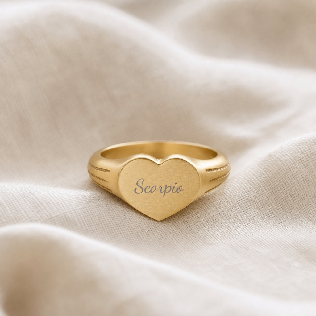 Scorpio zodiac heart signet ring linen flatlay — engraved Scorpio heart ring on rumpled cream linen with dried floral, editorial styling