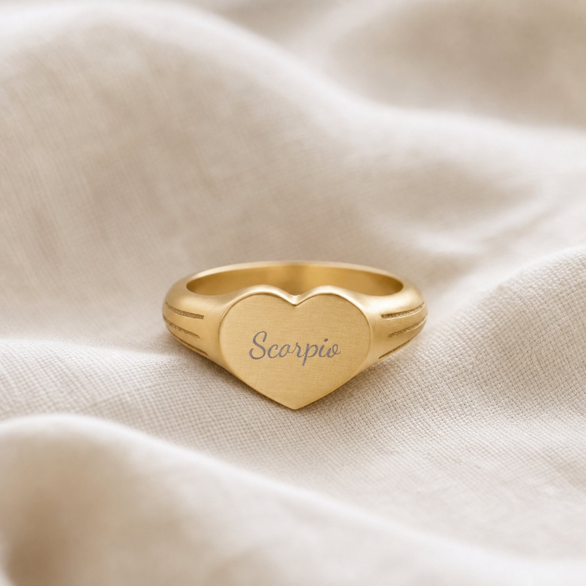 Scorpio zodiac heart signet ring linen flatlay — engraved Scorpio heart ring on rumpled cream linen with dried floral, editorial styling