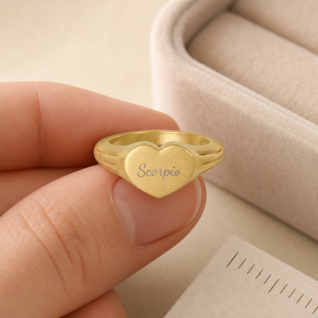 Scorpio zodiac heart signet ring scale-in-hand — fingers holding heart ring next to gift box and ruler, dainty signet sizing