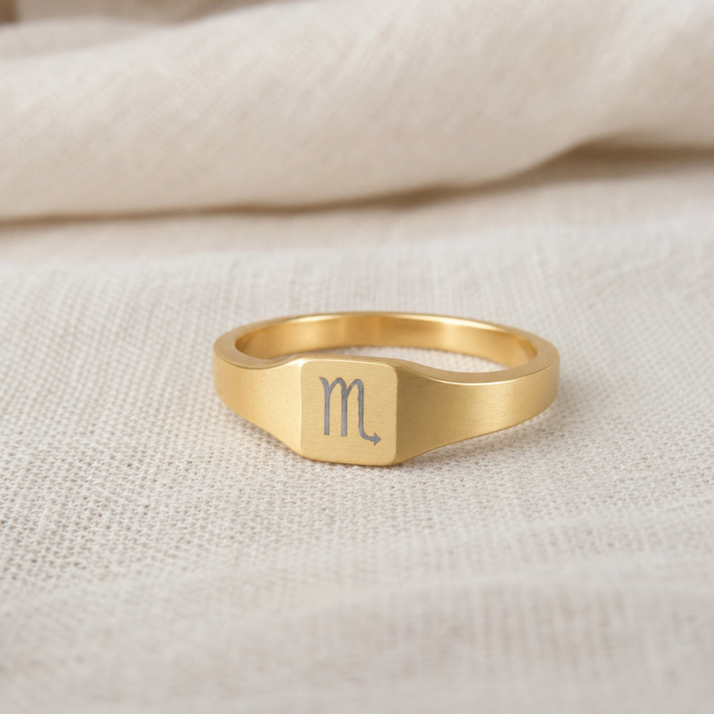 Scorpio zodiac square signet ring on finger — model wearing engraved Scorpio signet, cream linen lifestyle moment