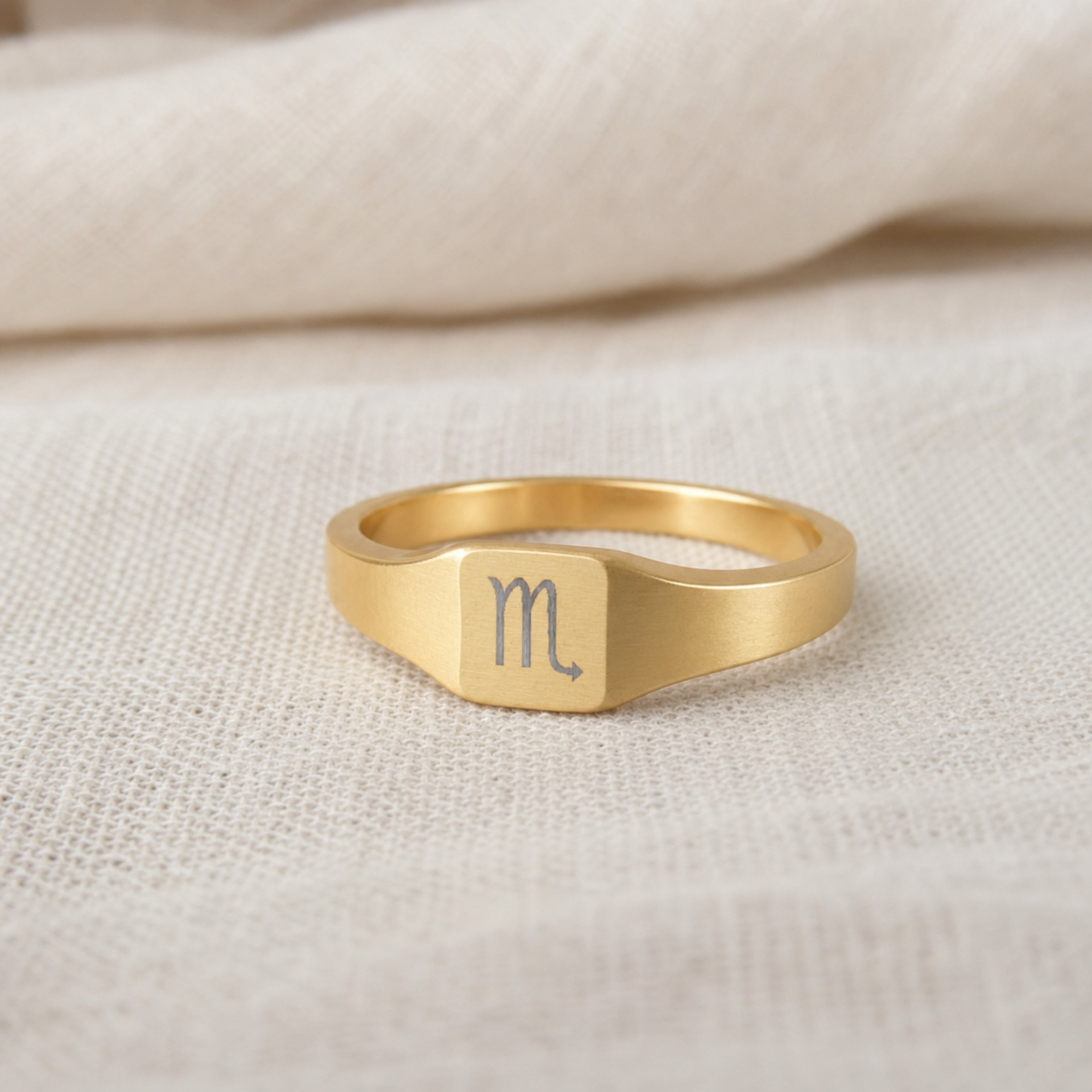 Scorpio zodiac square signet ring on finger — model wearing engraved Scorpio signet, cream linen lifestyle moment