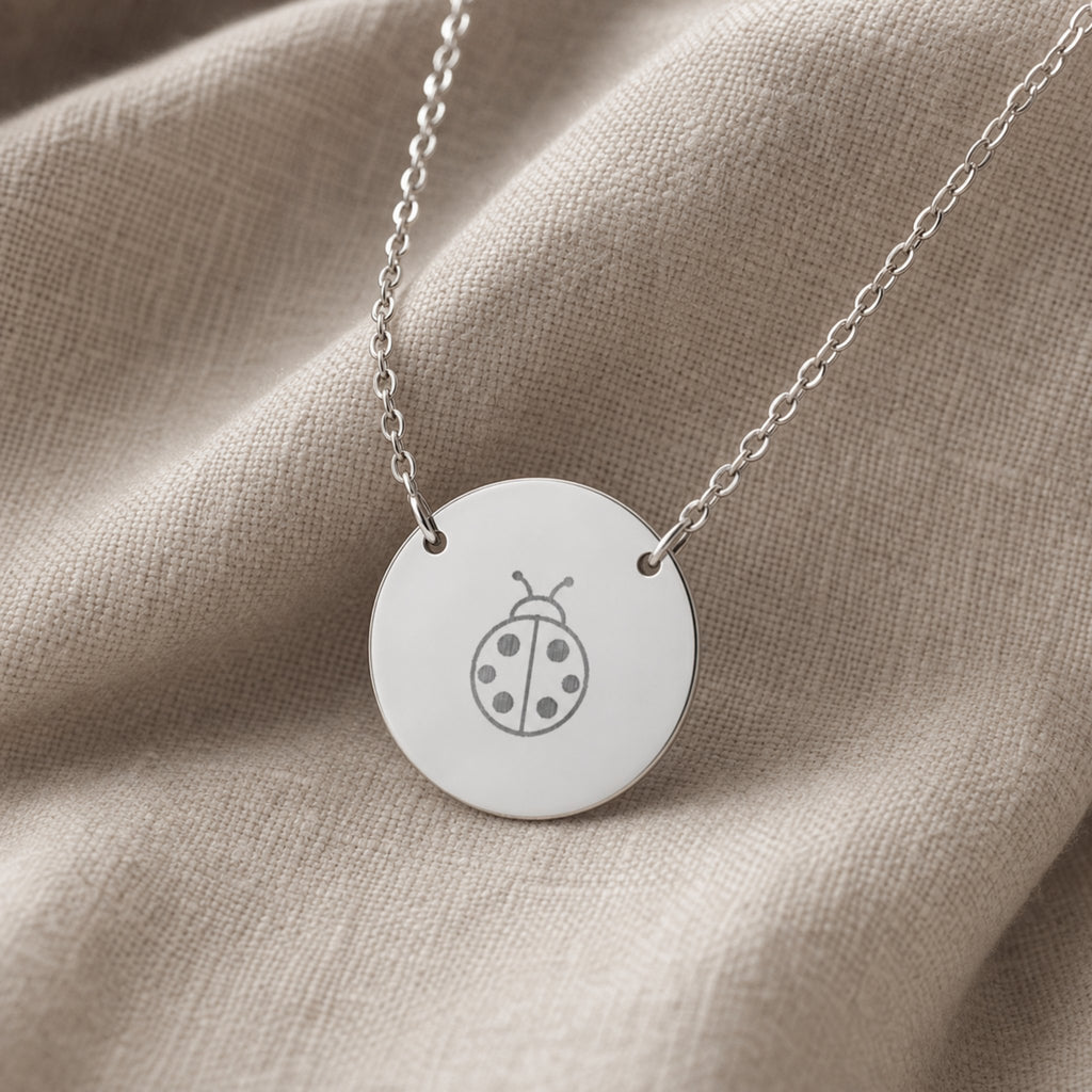 Dainty engraved ladybug coin necklace in stainless steel — laser-engraved ladybug on polished round pendant, clean editorial styling